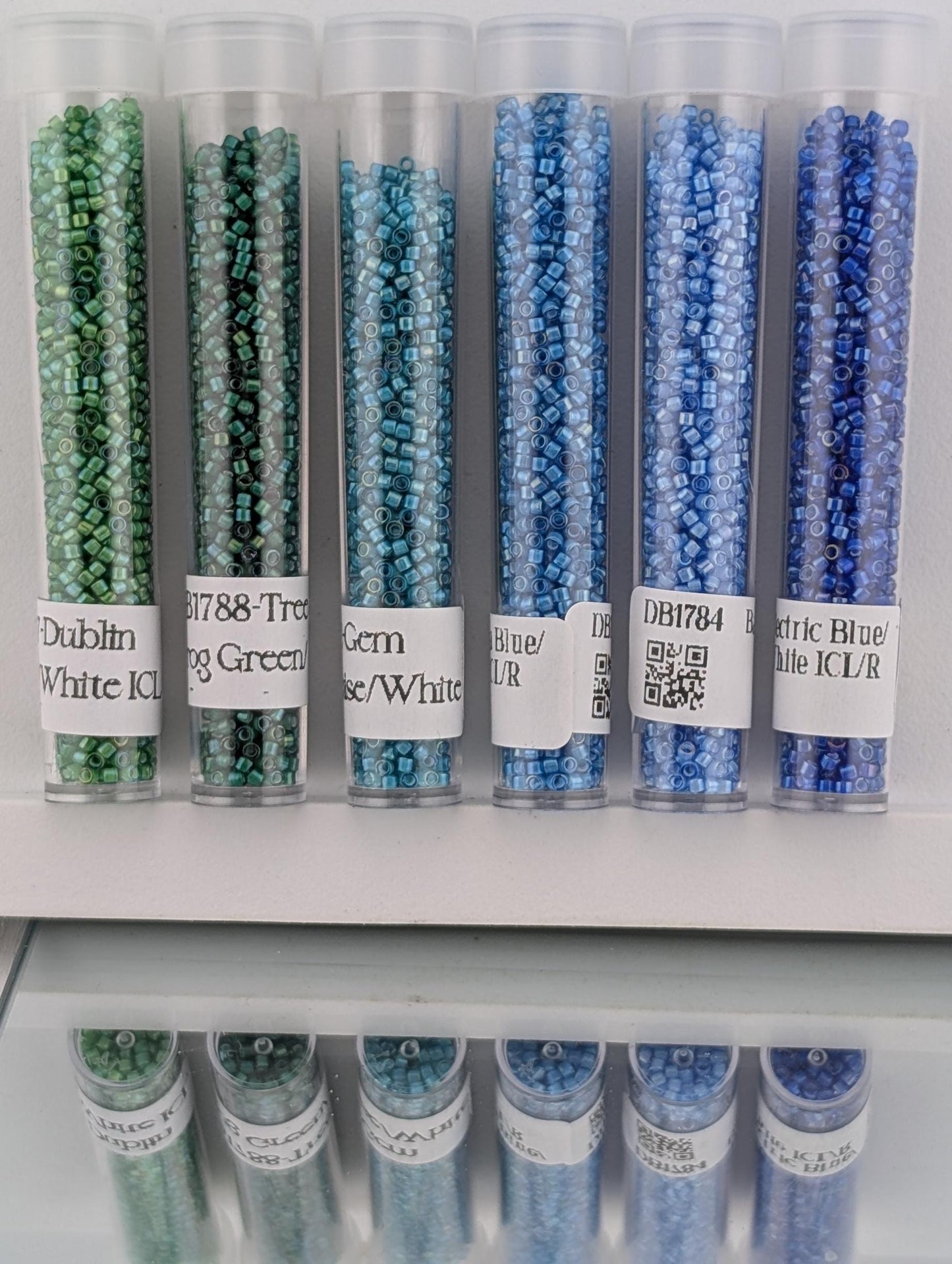a collection of six transparent glass containers filled with colorful beads, each labeled with a different color.