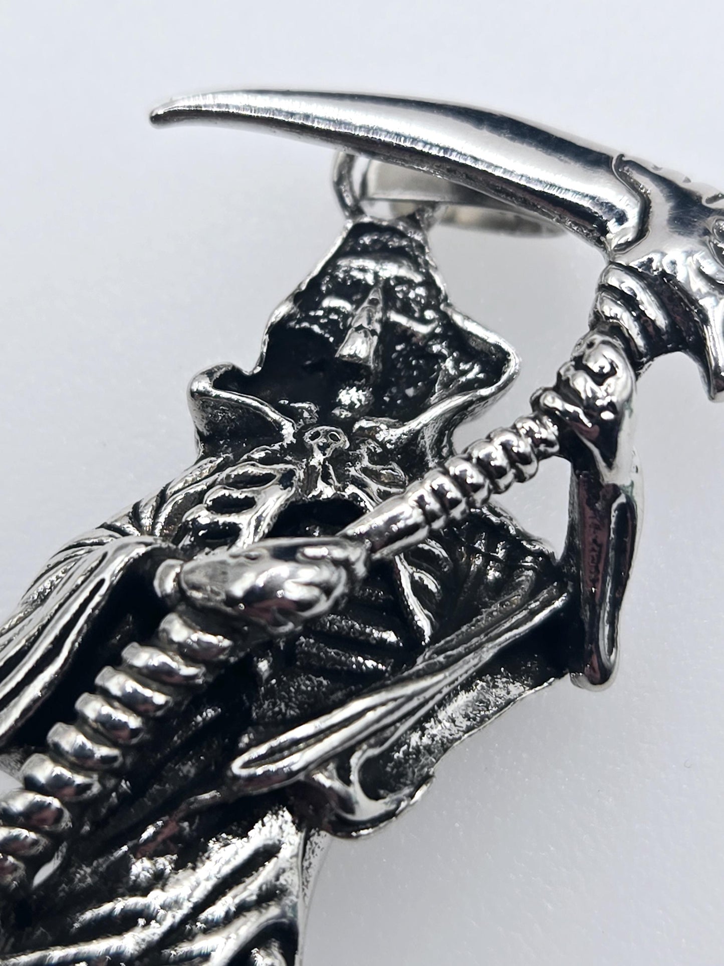 A close-up view of a silver metal sculpture depicting a skeletal or metallic creature with a pointed, curved blade-like object.