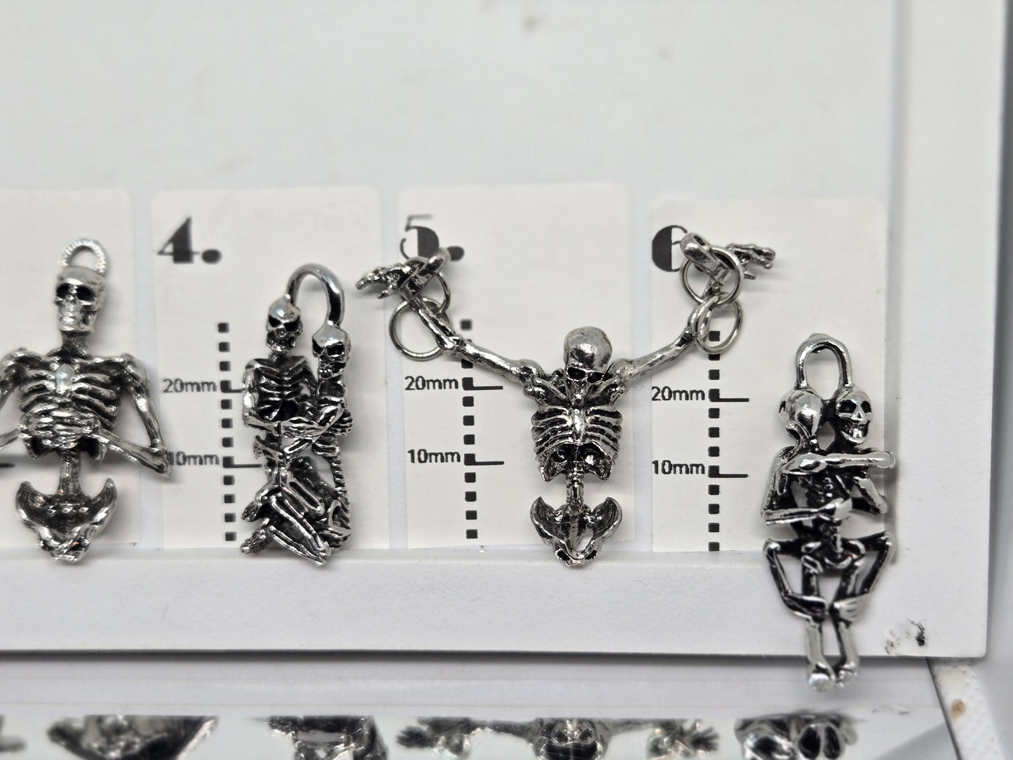 a collection of silver-colored metal charms, including skull-shaped pendants, arranged on a white surface.