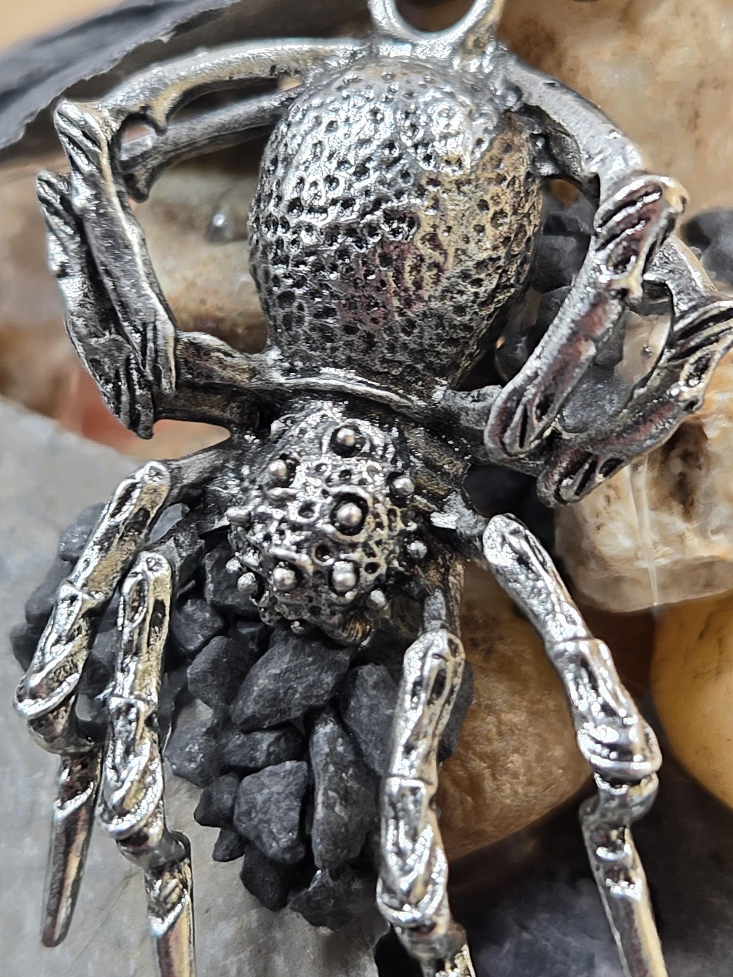 A close-up image of a detailed metal spider pendant, featuring intricate patterns and textures.