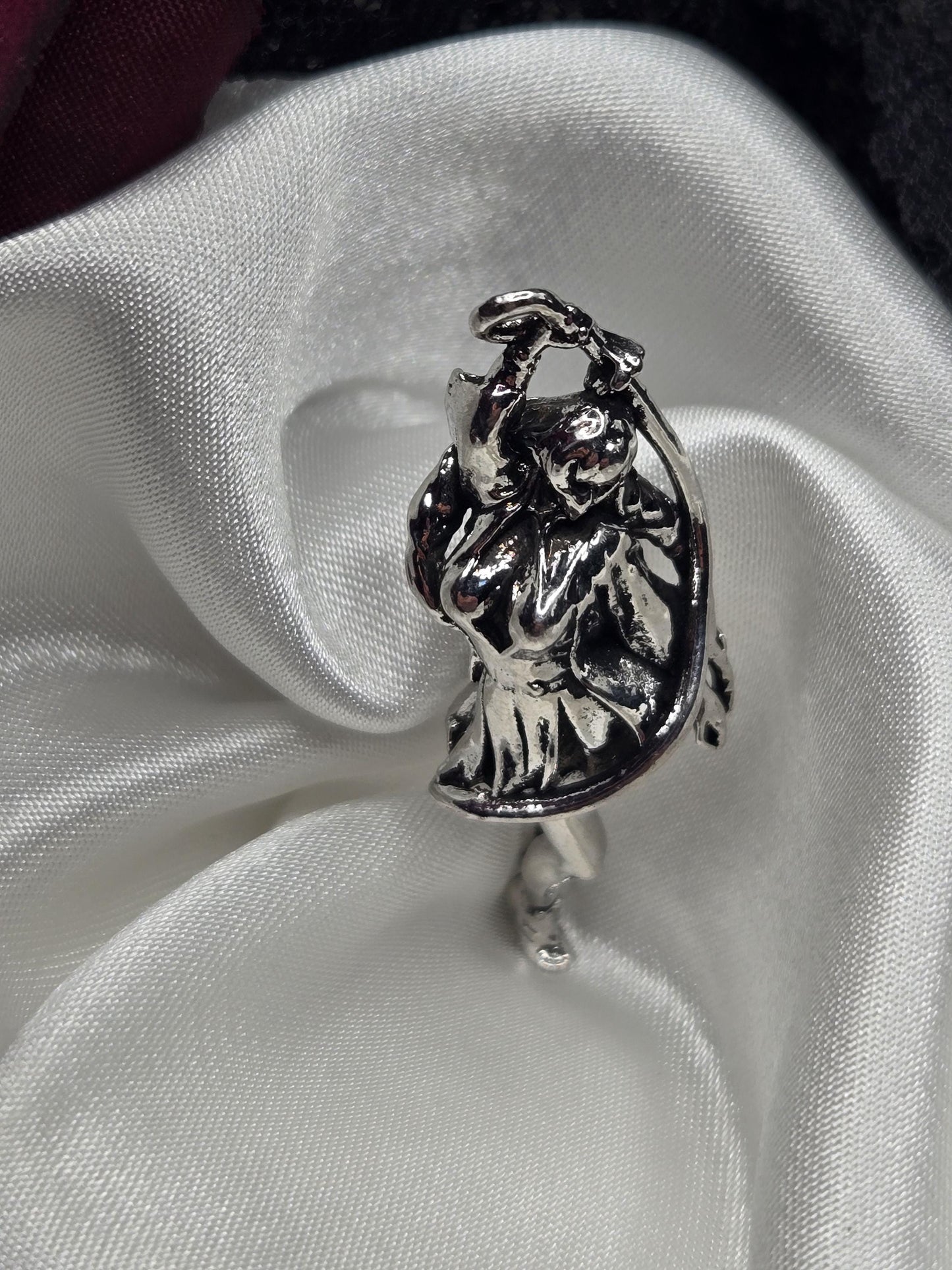 A silver-colored metal object, possibly a ring or a decorative piece, is resting on a white fabric surface.