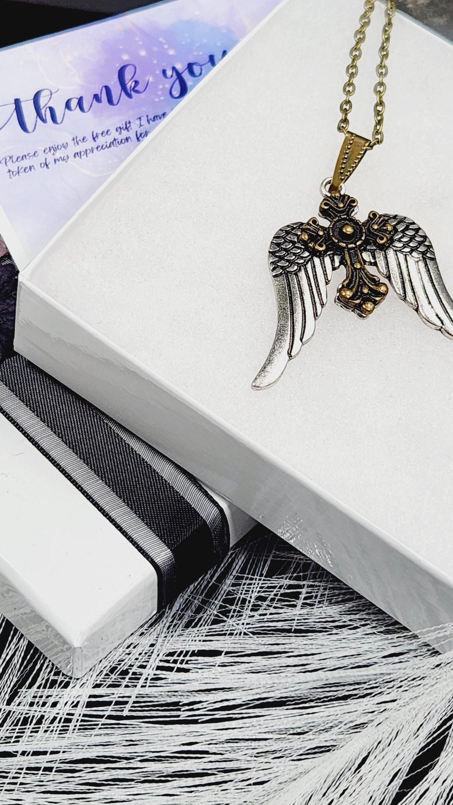 A white box with a gold cross pendant and a feather-like object on top, along with a purple card with text.