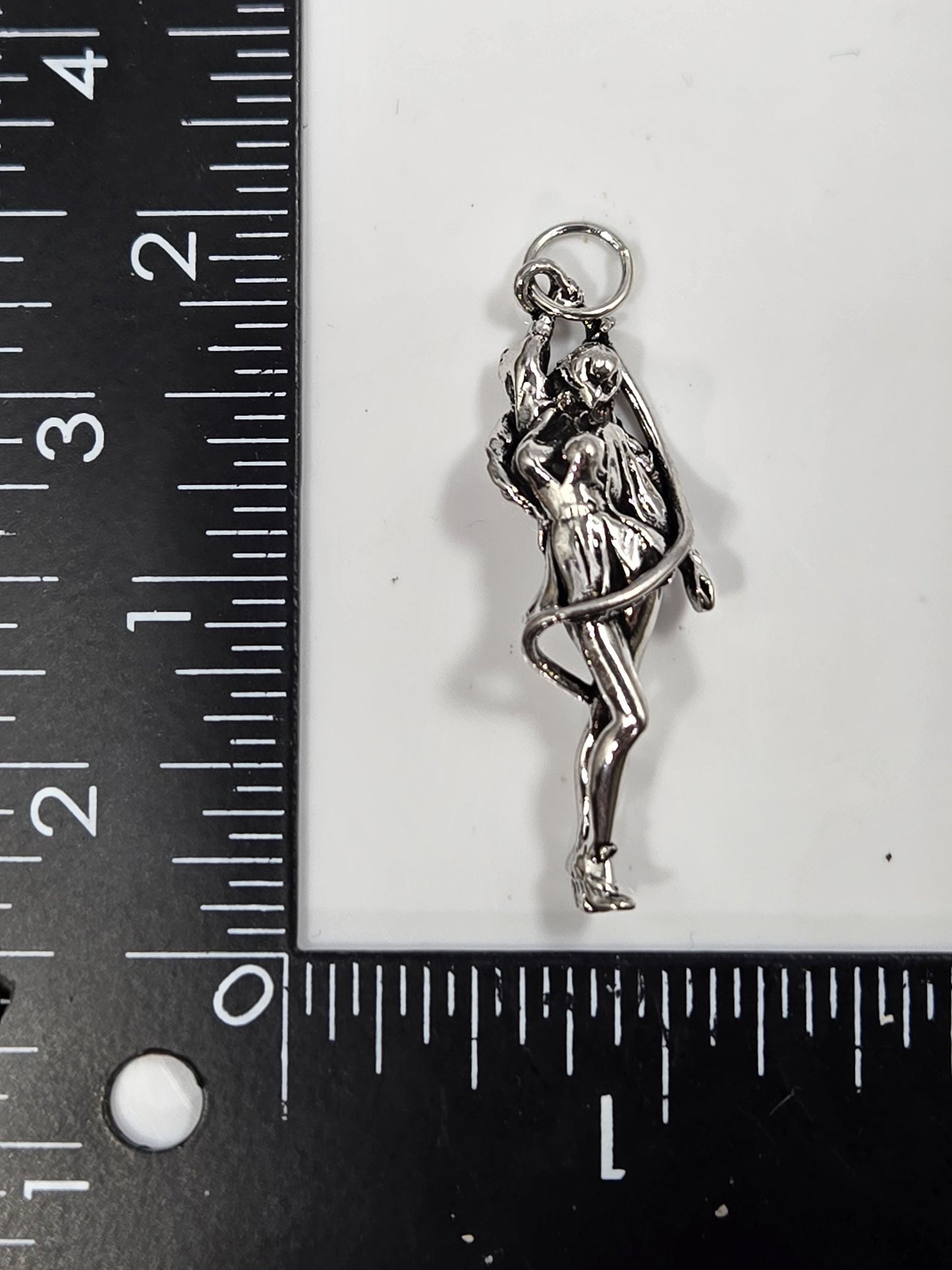 A silver-colored charm in the shape of a woman is placed next to a ruler on a black surface.