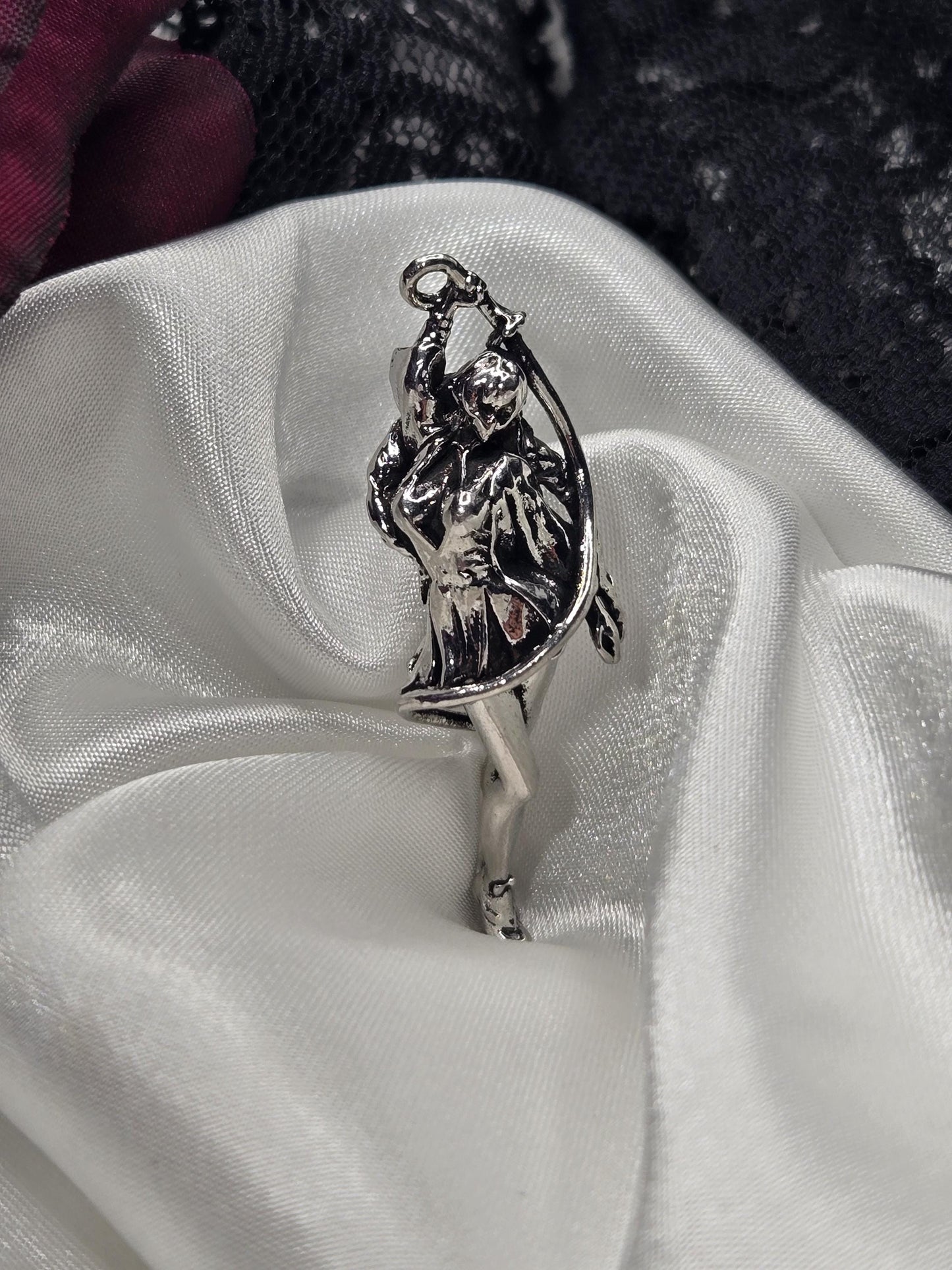 A silver-colored metal charm or pendant is resting on a white fabric surface.
