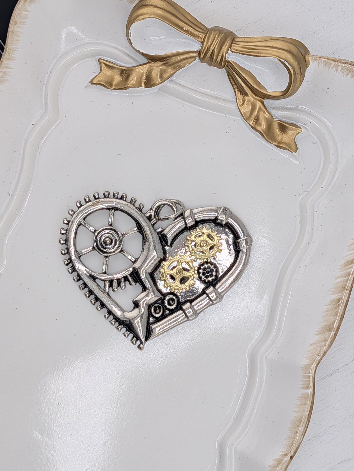 a heart-shaped metal piece with gears and a ribbon bow on a white surface.
