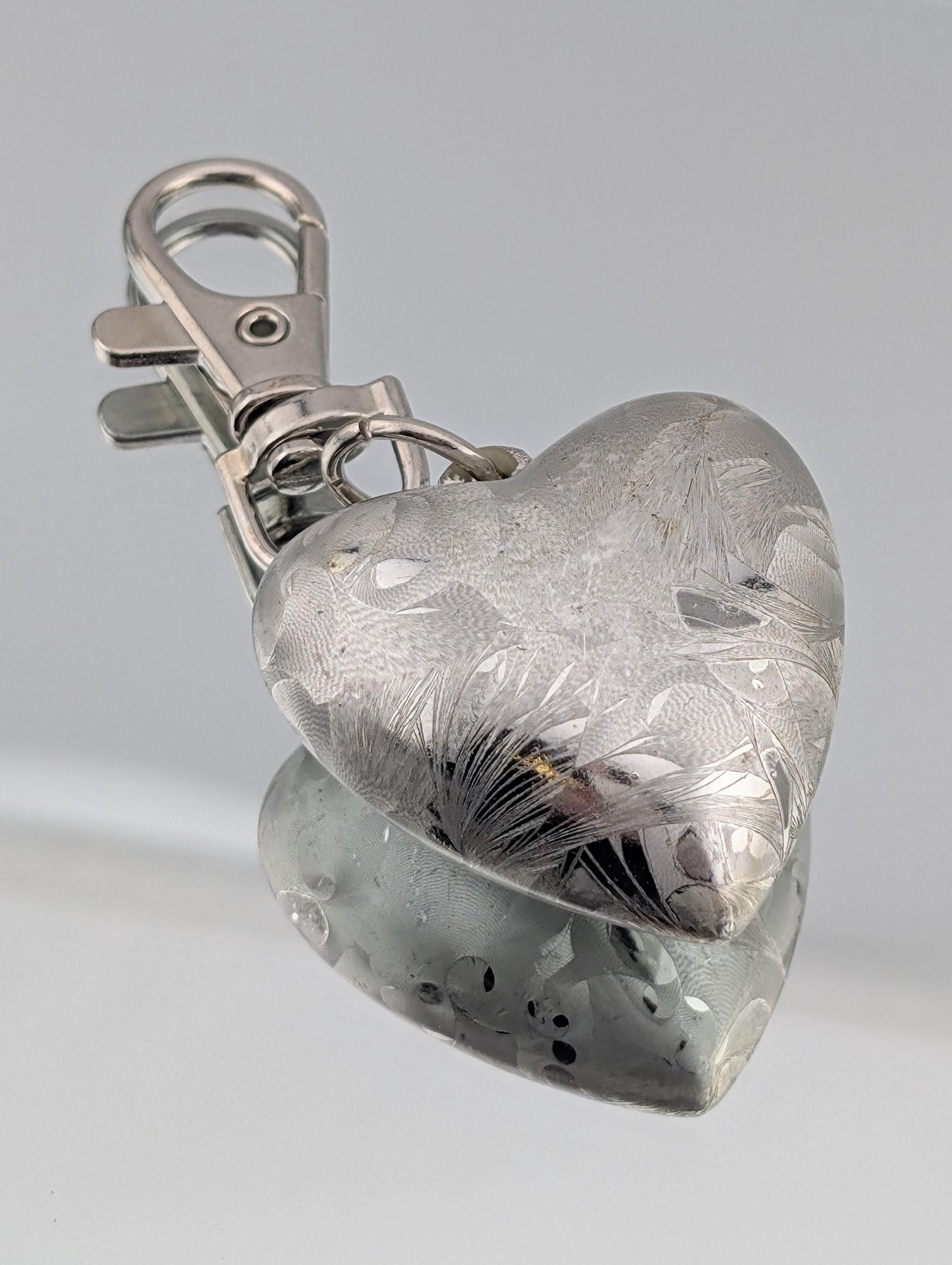 A silver heart-shaped keychain with a metal clasp and a reflective surface.
