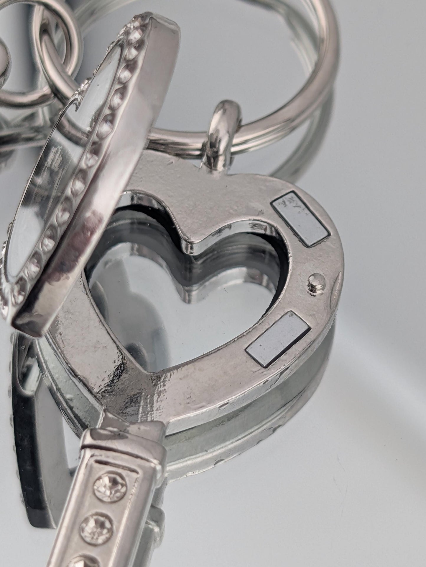 A close-up view of a heart-shaped keychain with a reflective surface, featuring a keyring and a key attached to it.