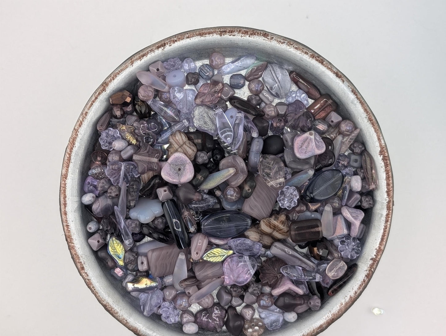 A bowl filled with various colorful beads, including purple, black, and multicolored stones, is shown in the image.