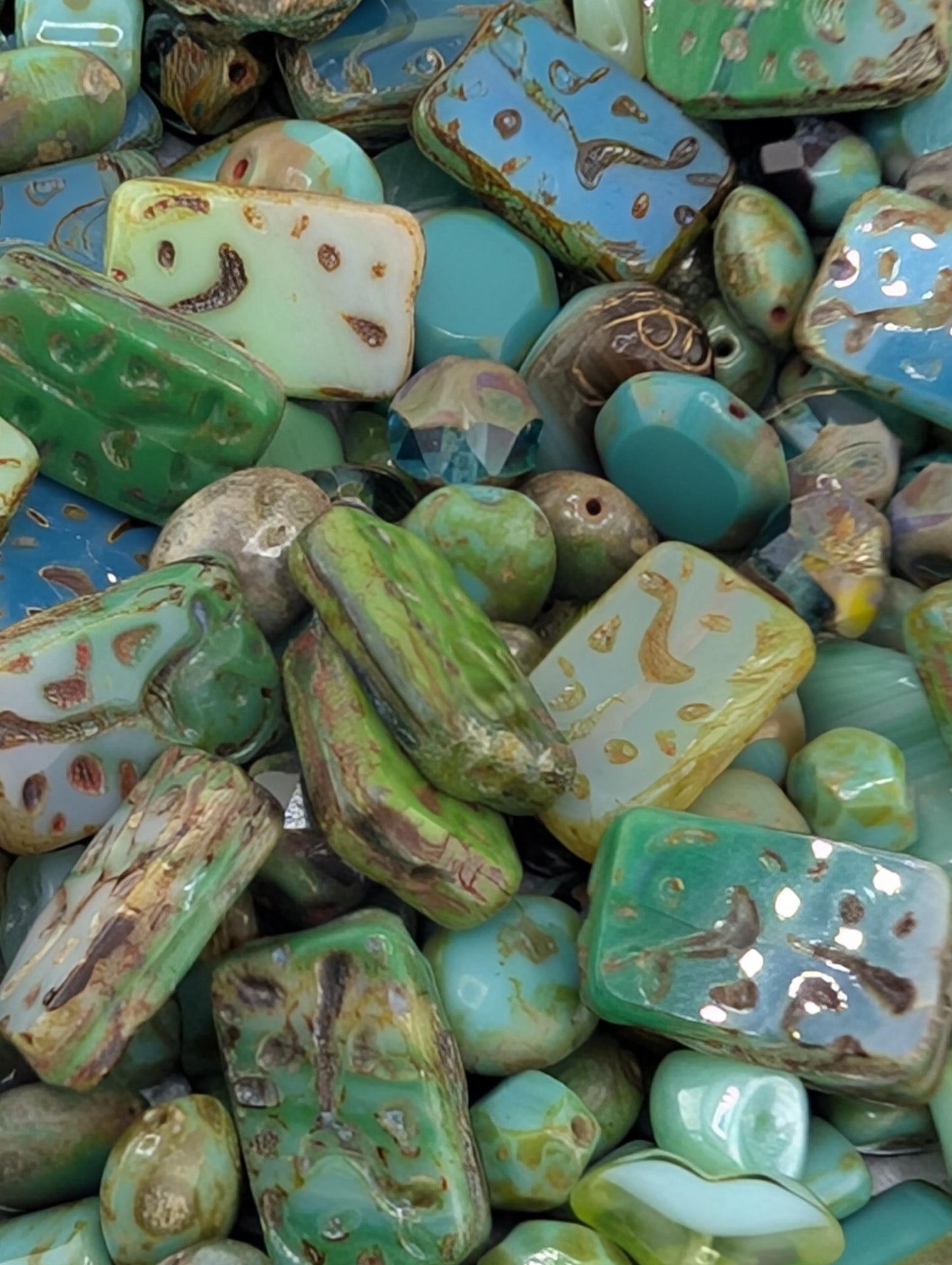 The image is a close-up of various colorful beads and stones, including turquoise, green, and yellow stones, as well as some blue and white beads.