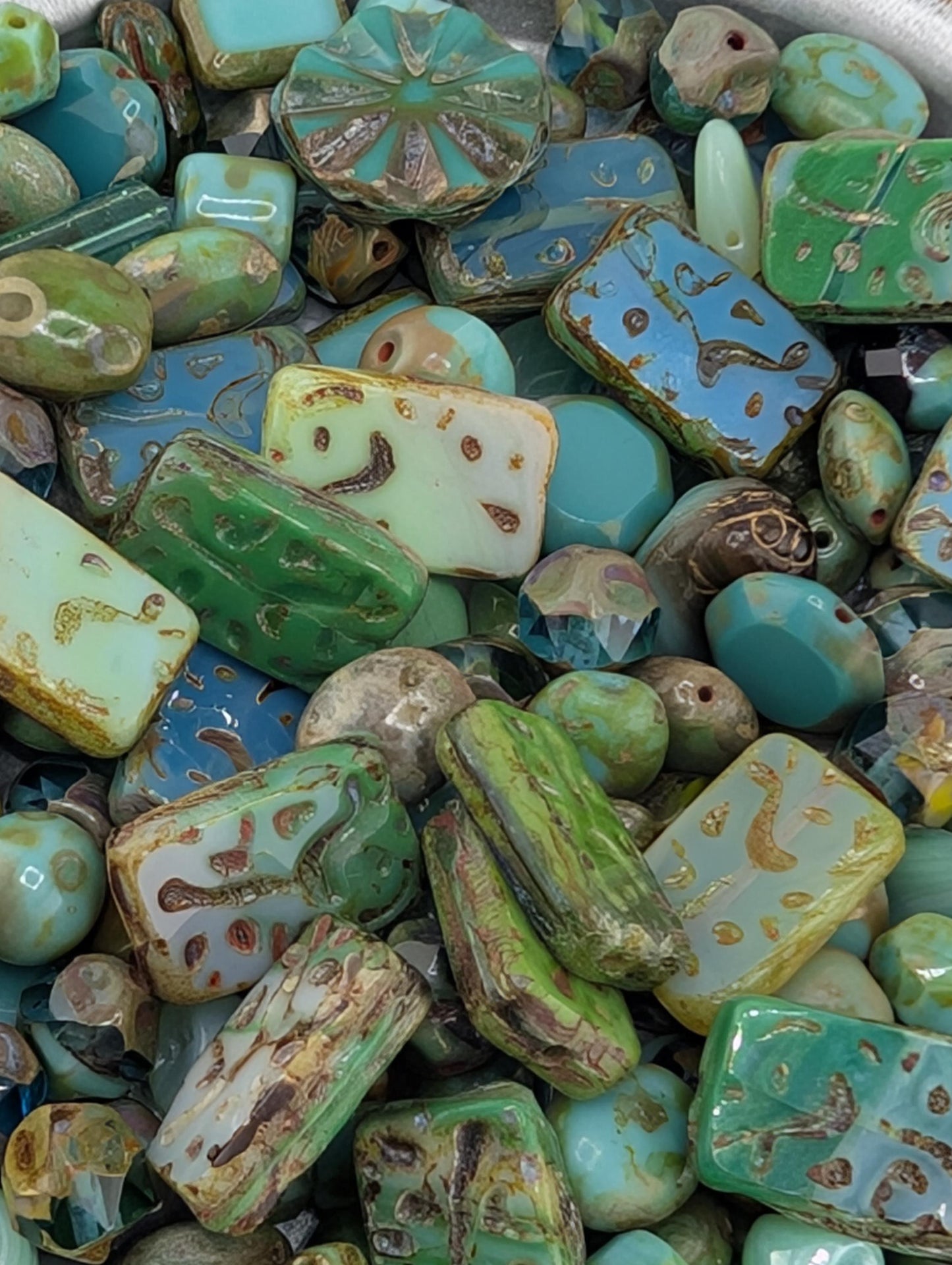 The image is a close-up of a collection of various colored glass beads, including green, blue, and yellow beads, as well as some with intricate designs.
