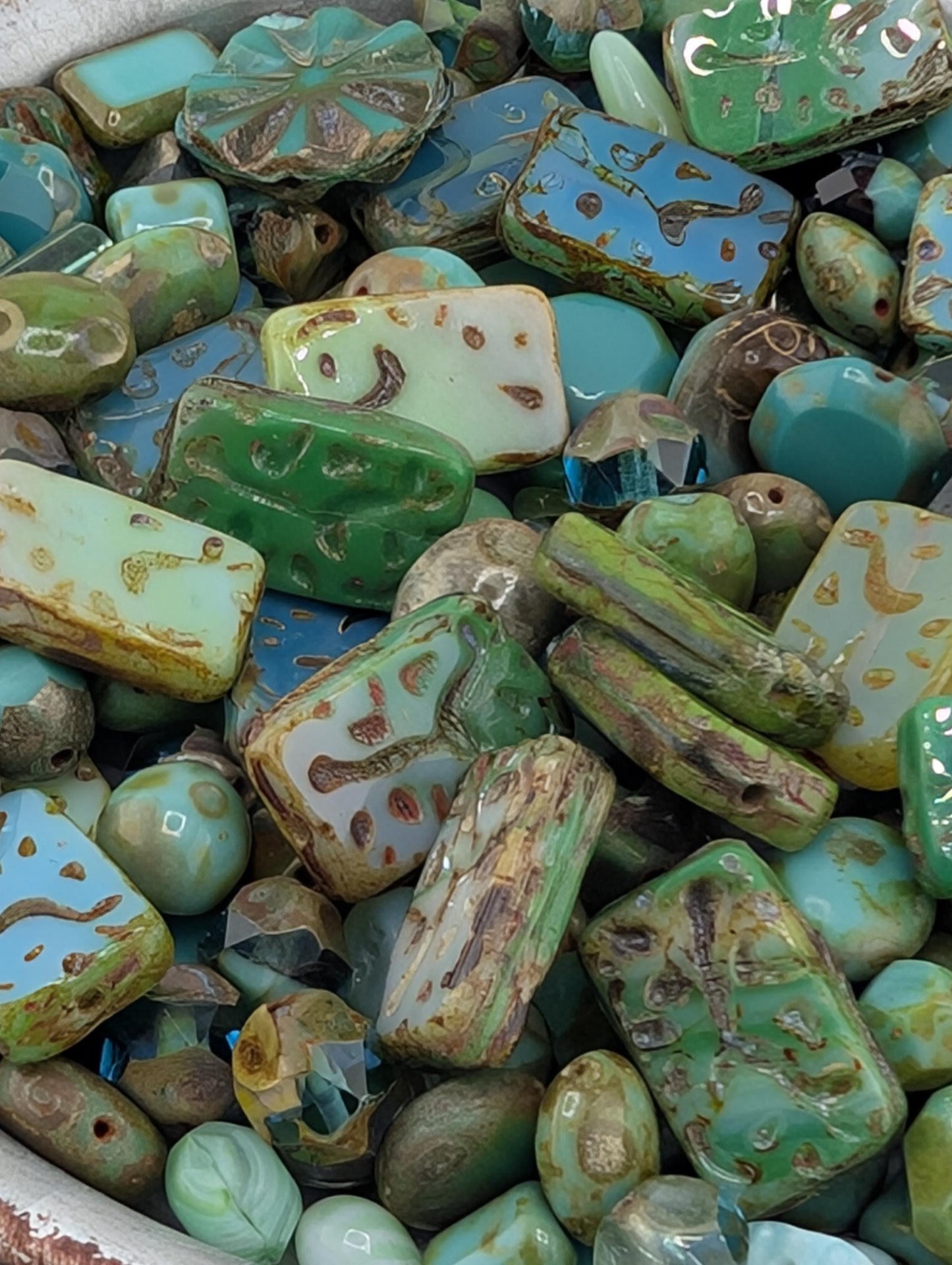 The image is a close-up view of a collection of various colored beads and stones, including turquoise, green, and blue hues.