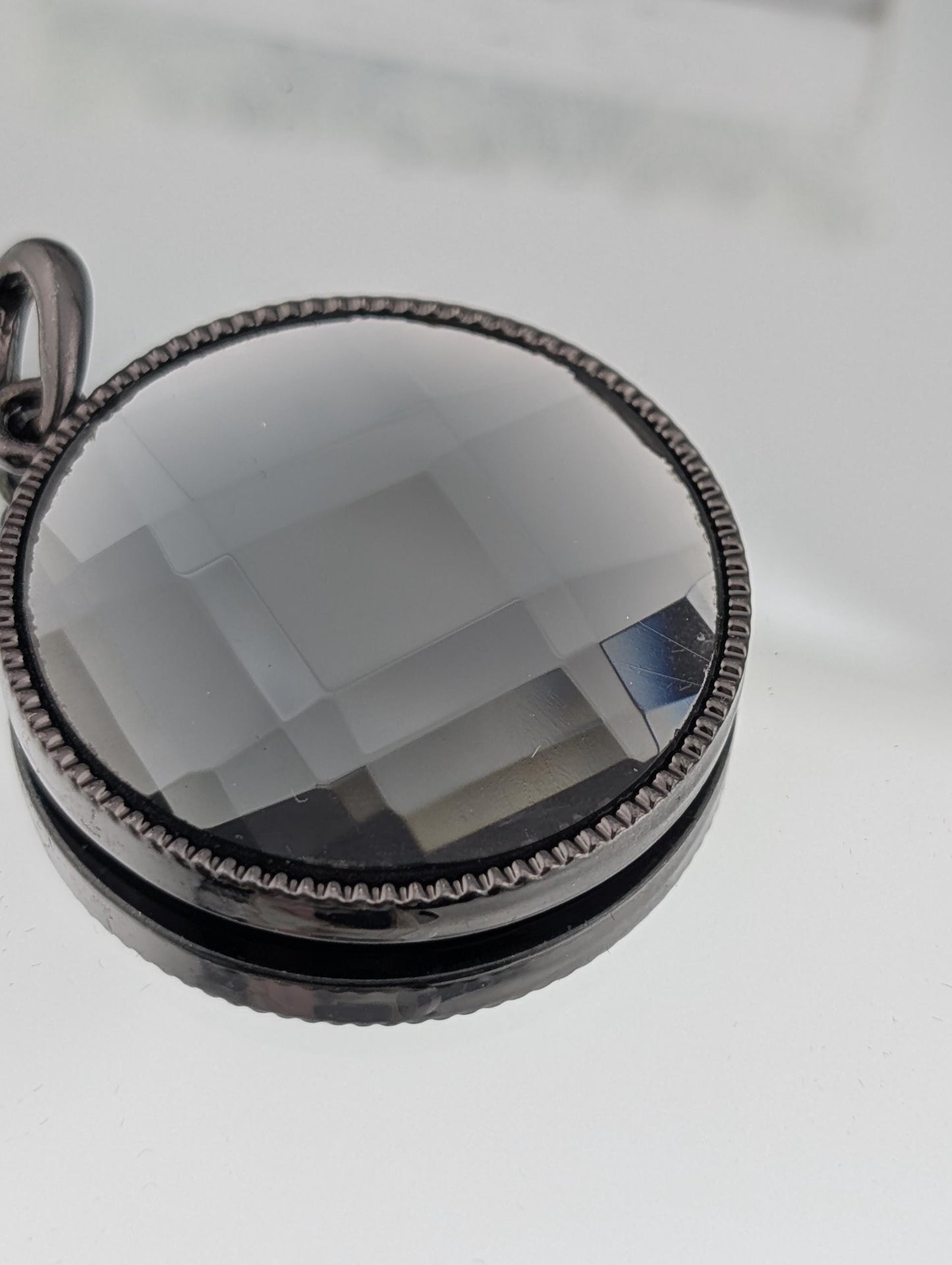 A close-up view of a round, black, and silver pendant with a clear, multicolored glass or crystal embedded in it.