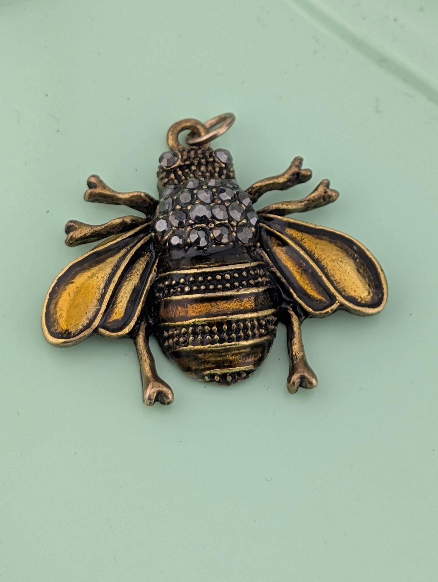 A decorative metal charm in the shape of a bee, with intricate details and a sparkling design.