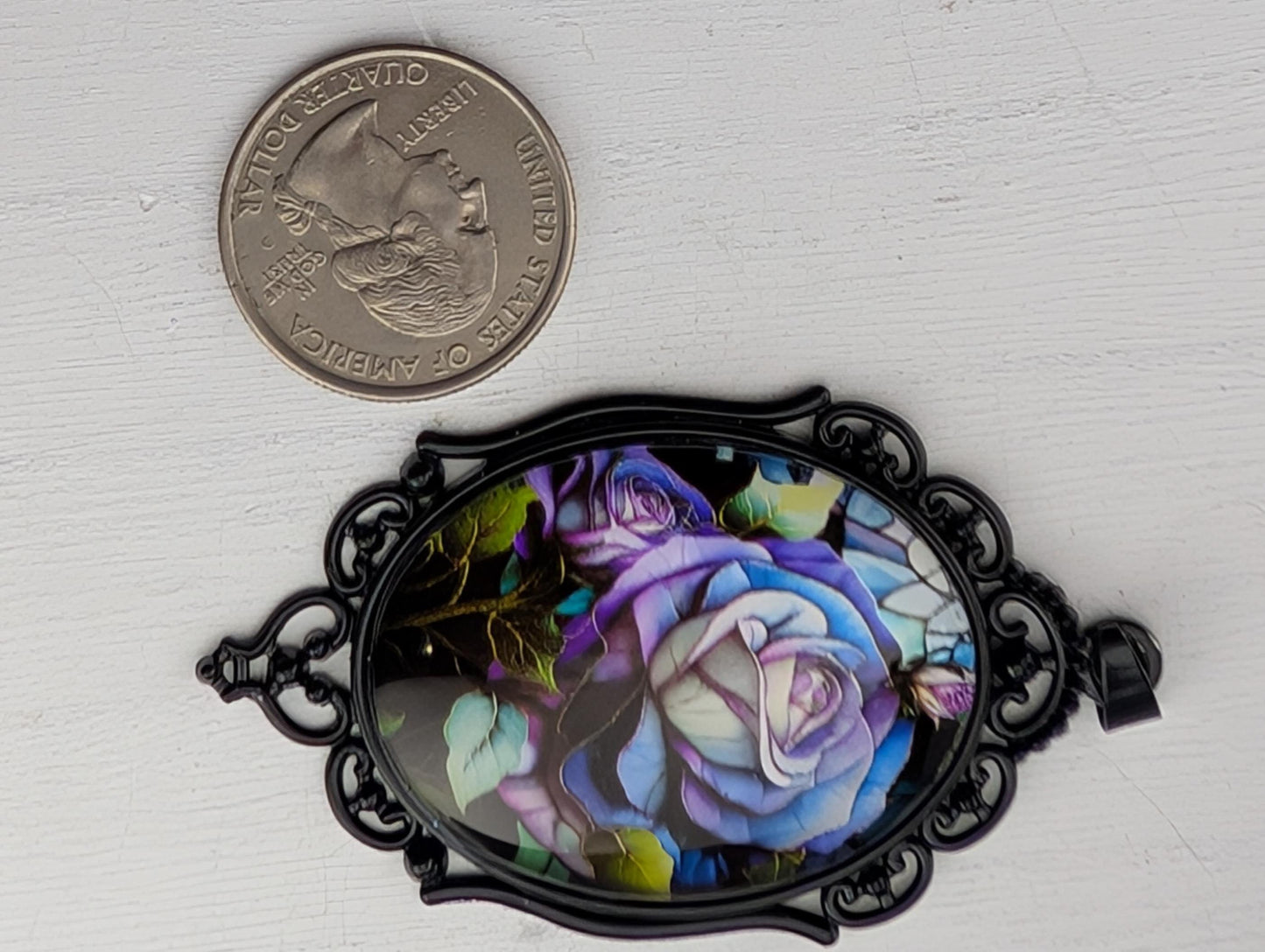 a decorative pendant with a floral design, placed next to a United States quarter coin.
