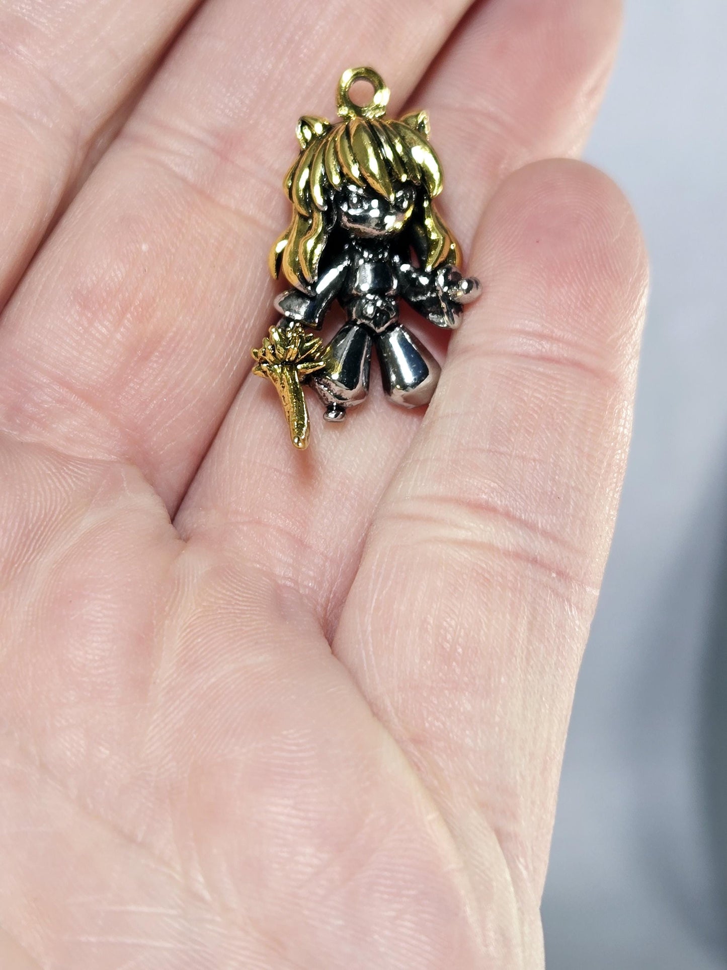 A hand holding a small, ornate charm in the shape of a bird or a similar figure.