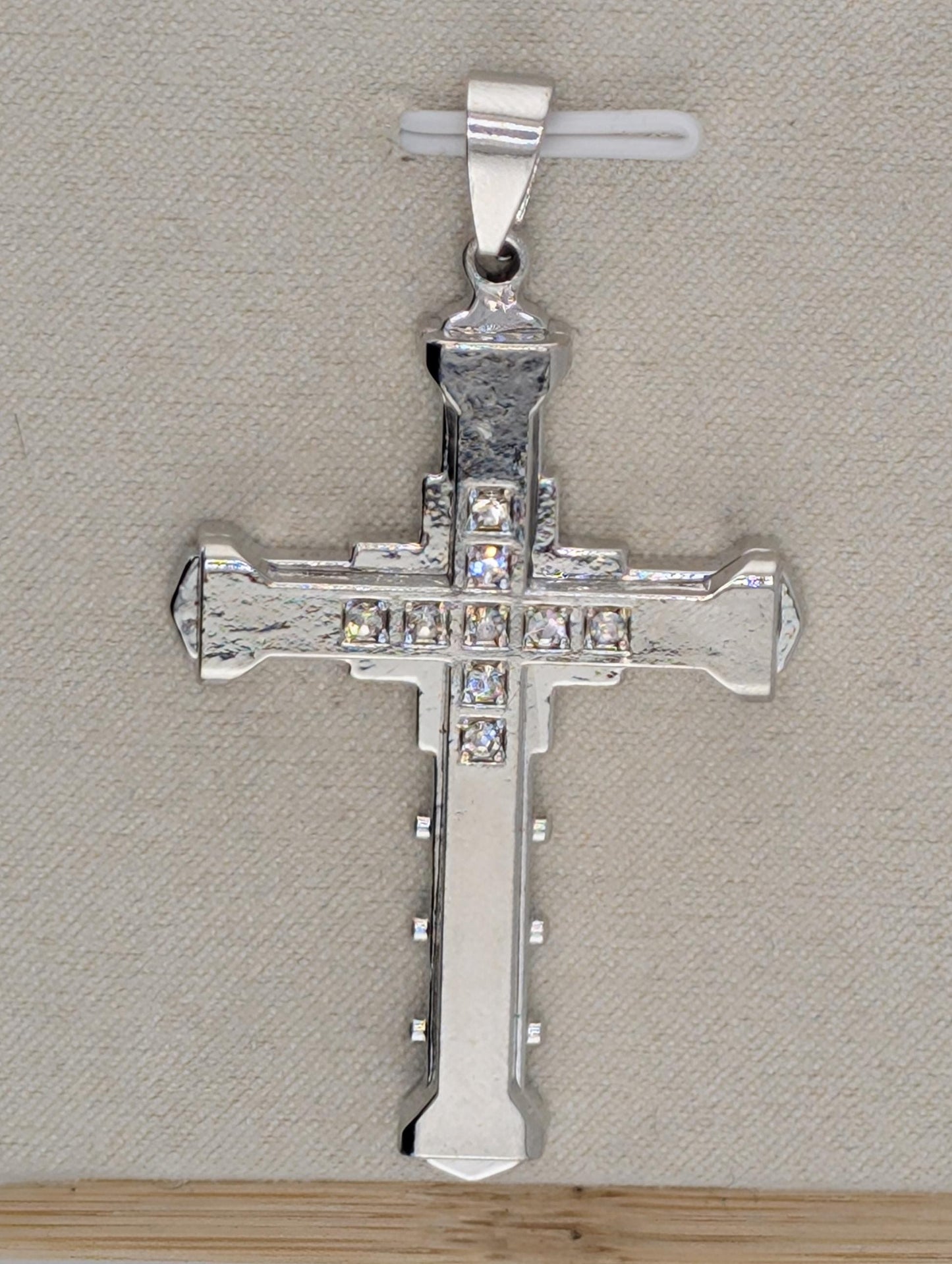 A silver-colored cross pendant with small diamonds or crystals embedded in it, hanging from a metal clasp.