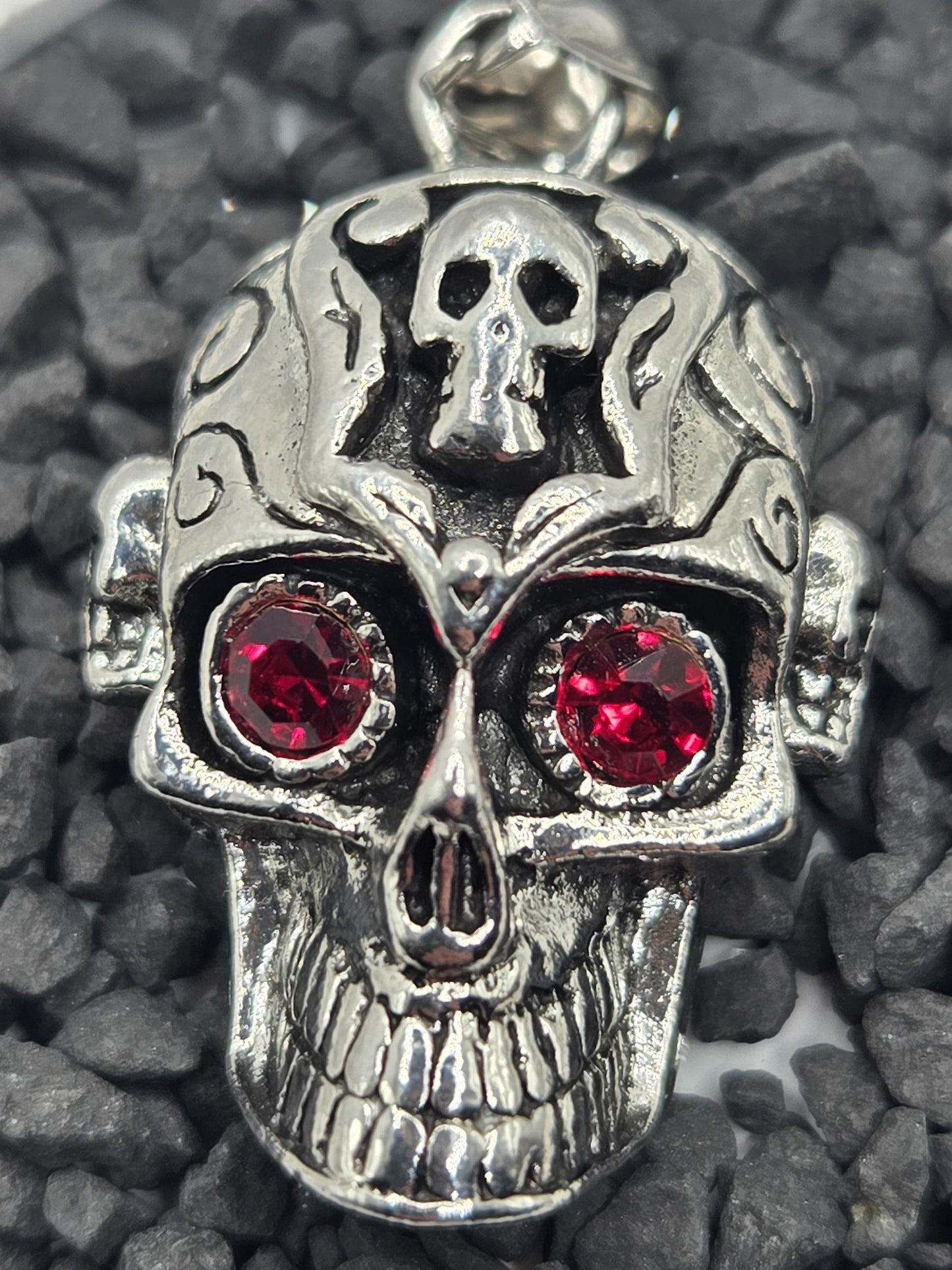 A silver-colored metal skull pendant with red gemstones, including two large red gemstones, is the main focus of the image.