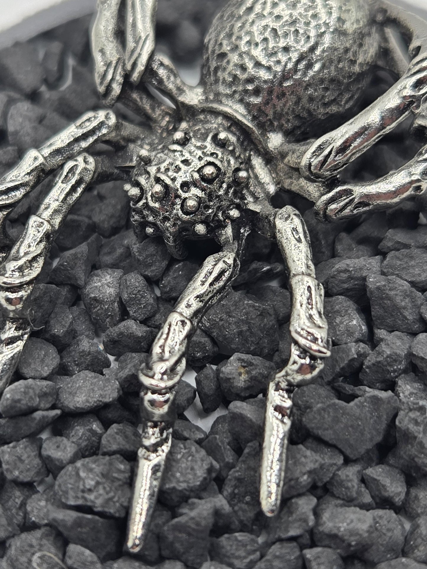 A close-up view of a metallic, spider-like object with intricate details, resting on a bed of small, dark rocks.