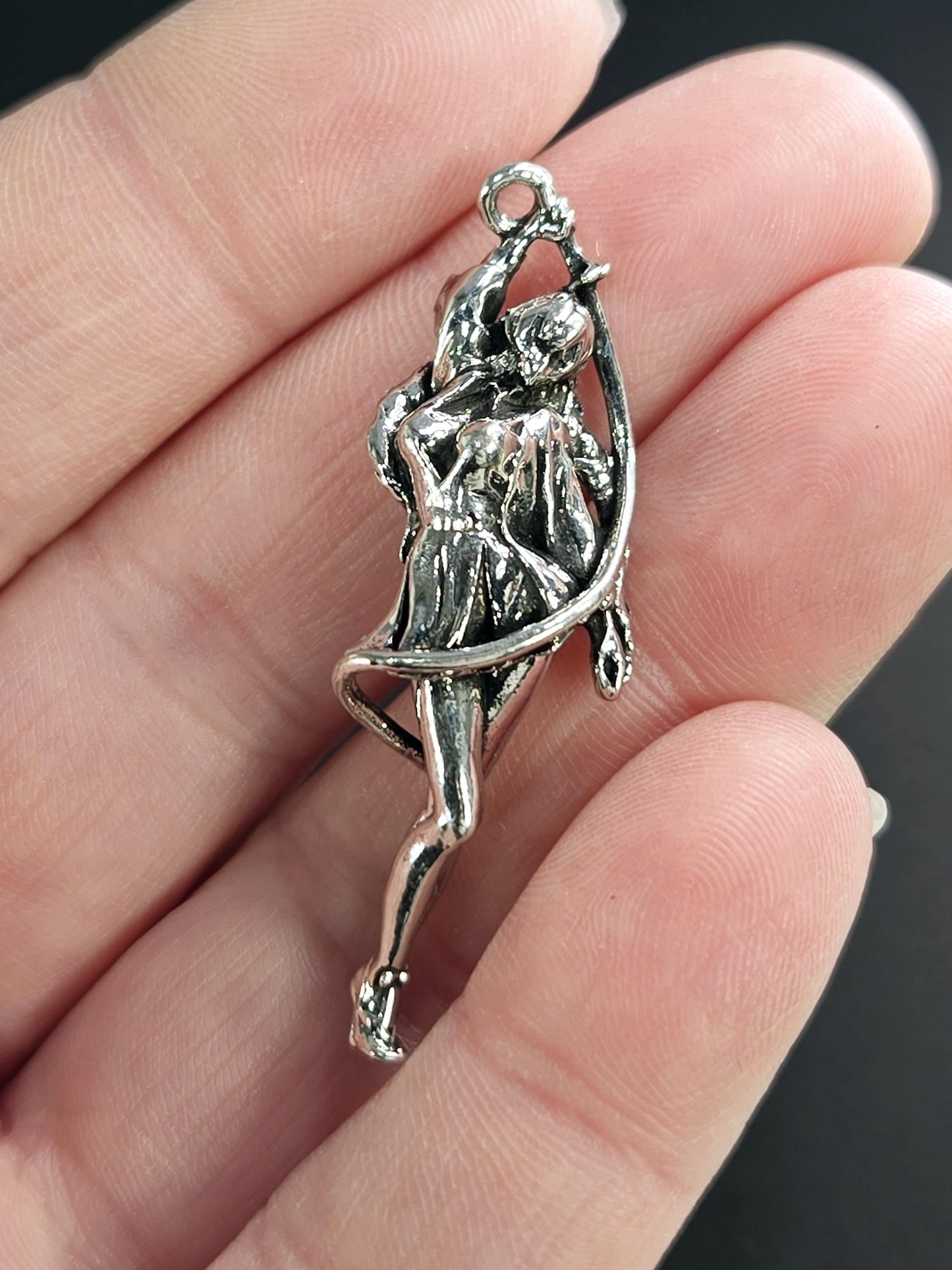 A close-up image of a person's hand holding a silver-colored pendant or brooch with an intricate design.