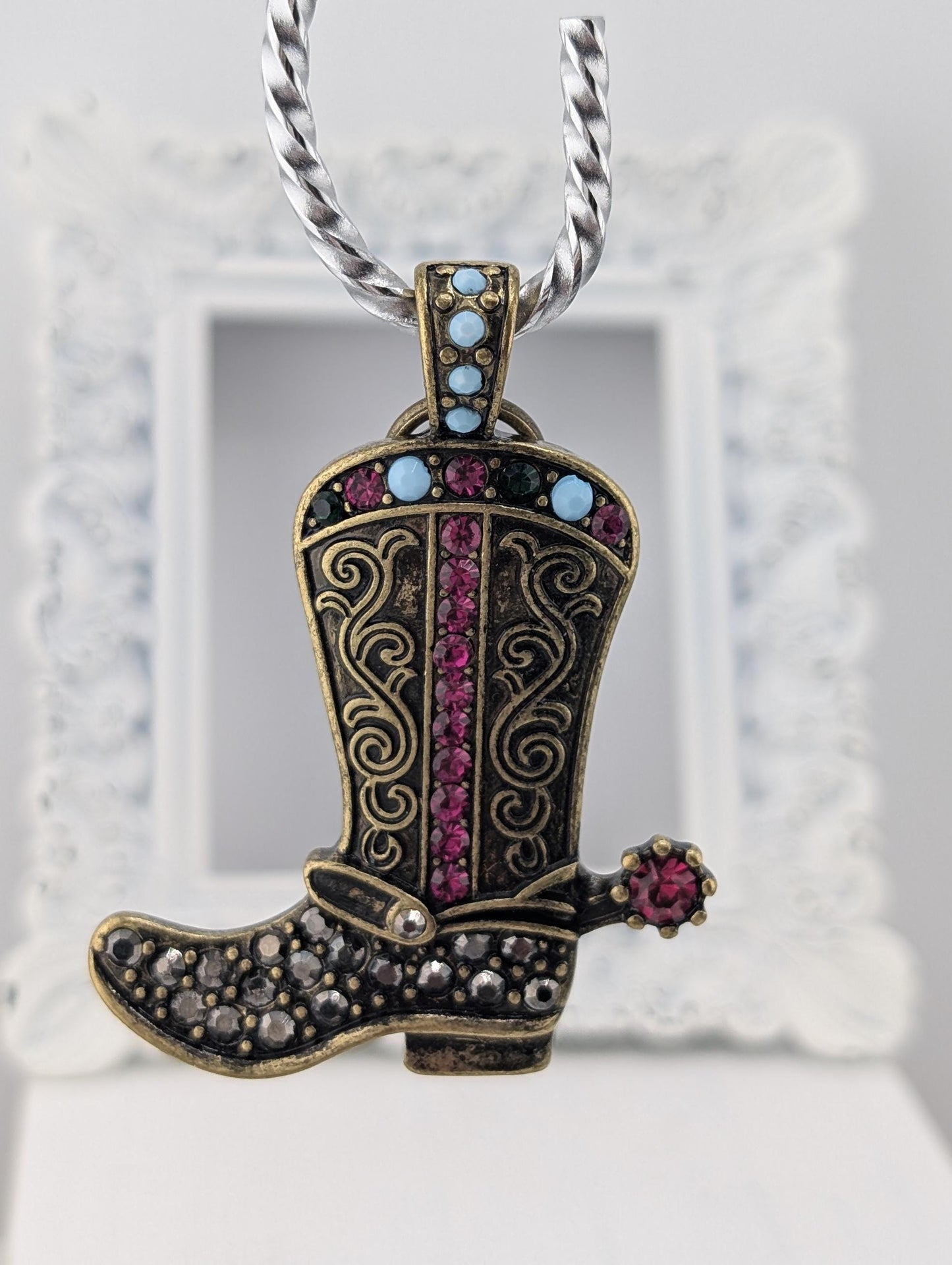 A decorative pendant in the shape of a cowboy boot, adorned with colorful gemstones and a chain.