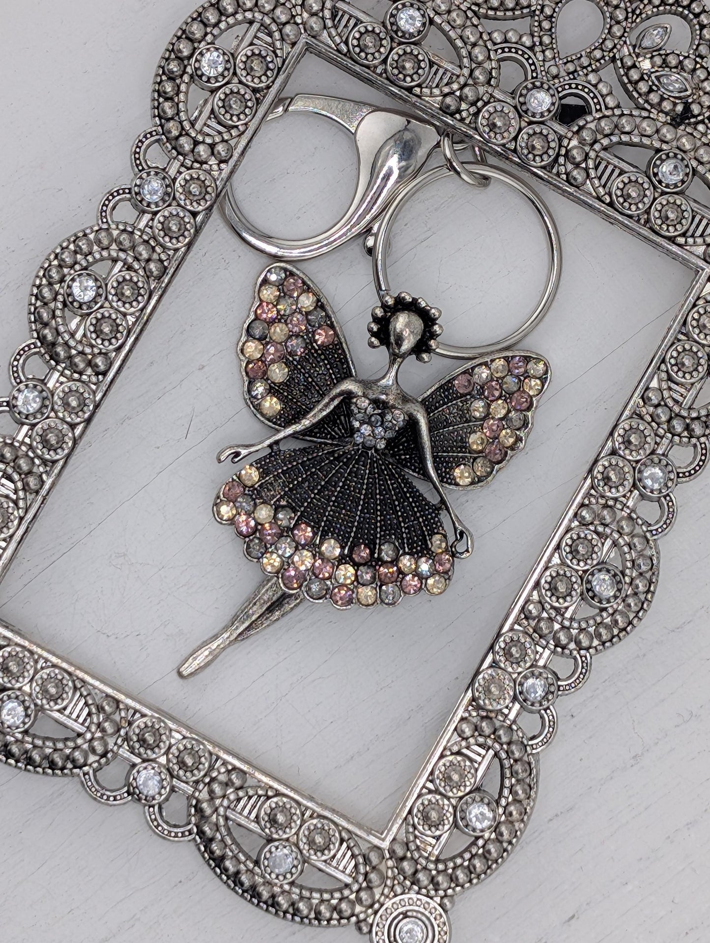 a silver-colored pendant with a butterfly design, adorned with sparkling rhinestones or crystals. The pendant is placed within an ornate, decorative metal frame, which adds an elegant touch to the overall presentation.