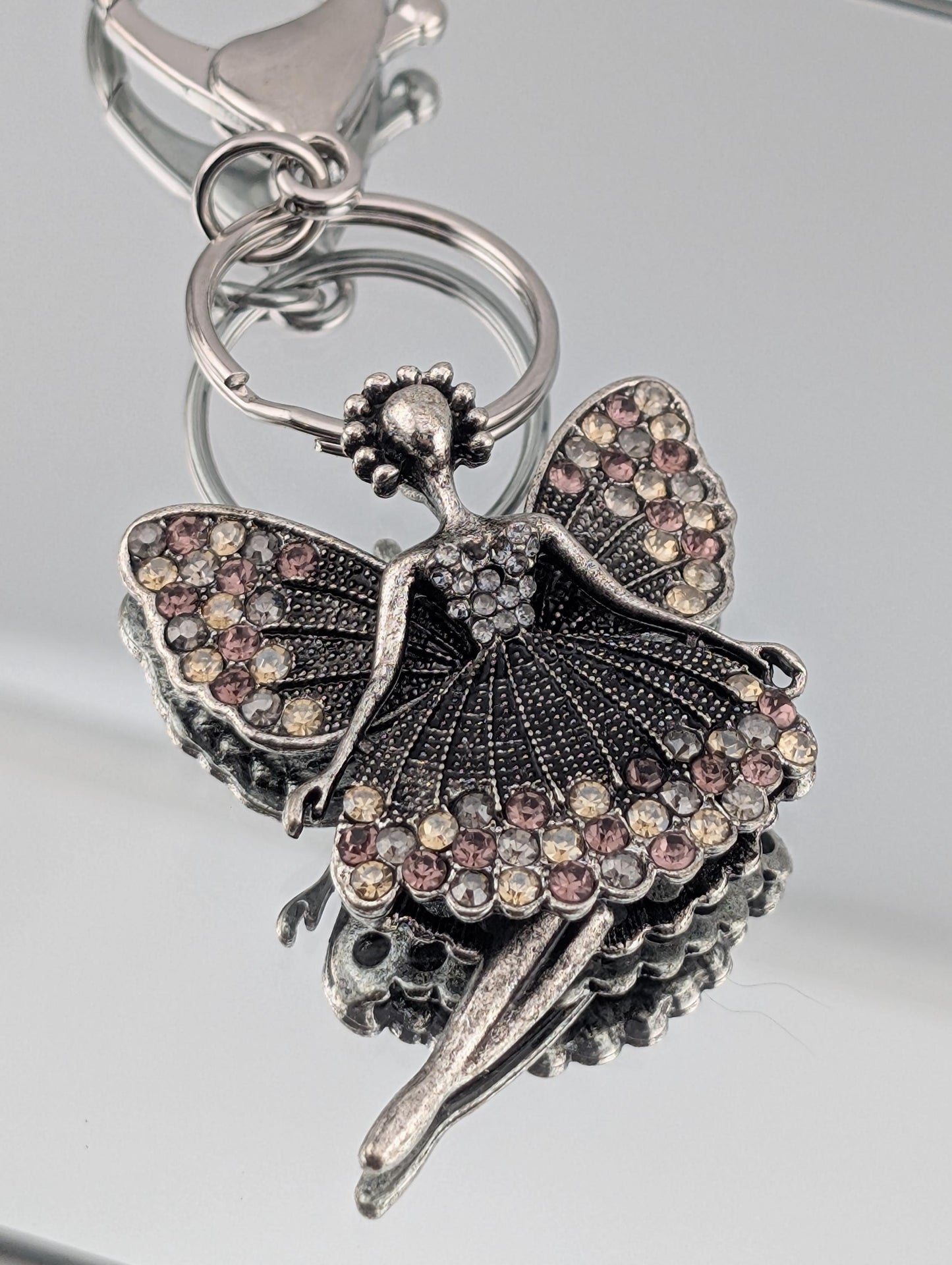 A silver-colored keychain with a decorative design featuring a butterfly-like figure with intricate details and sparkling gemstones.