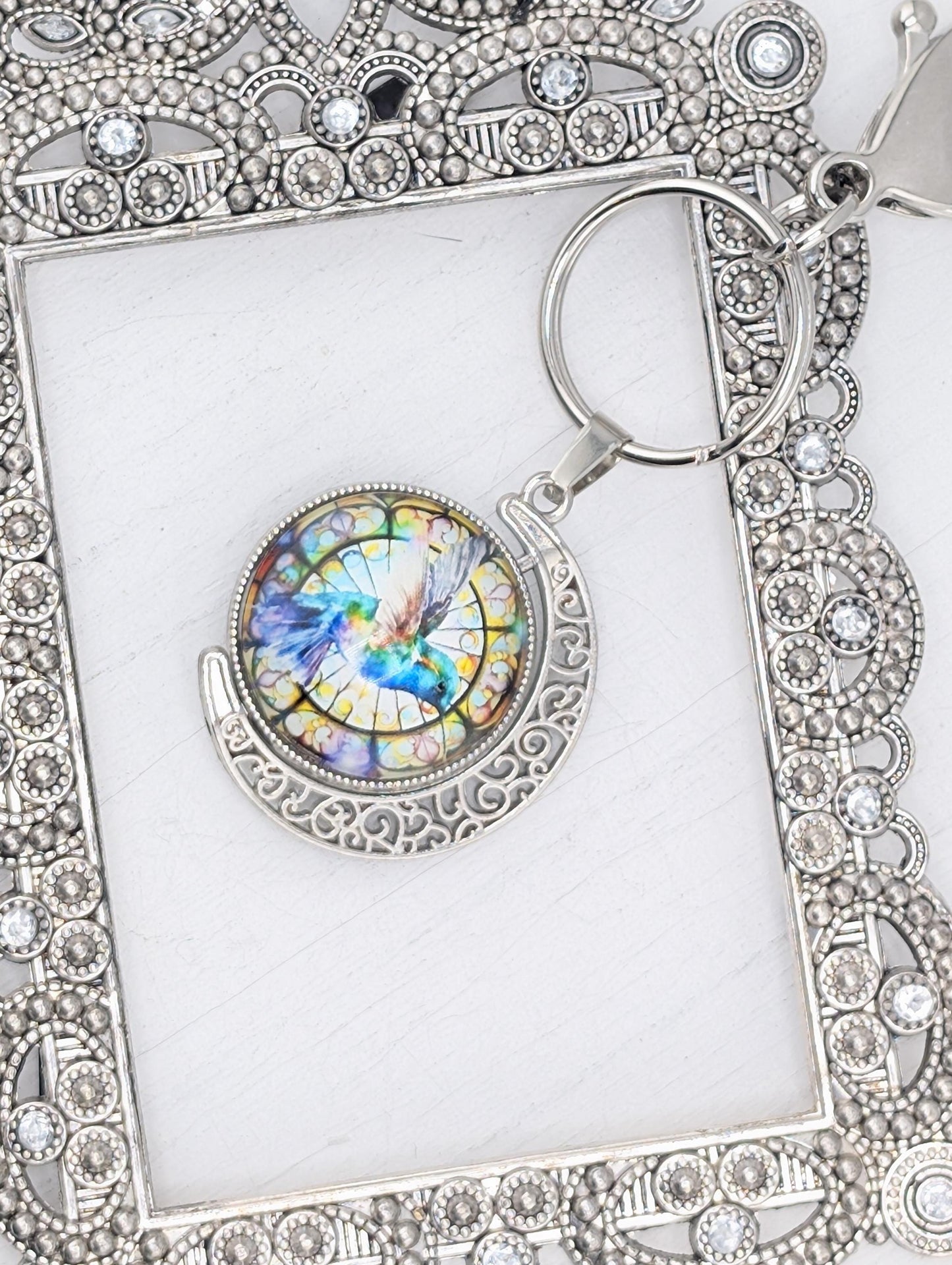 A decorative keychain with a colorful stained glass design featuring a bird, possibly a hummingbird, in the center.