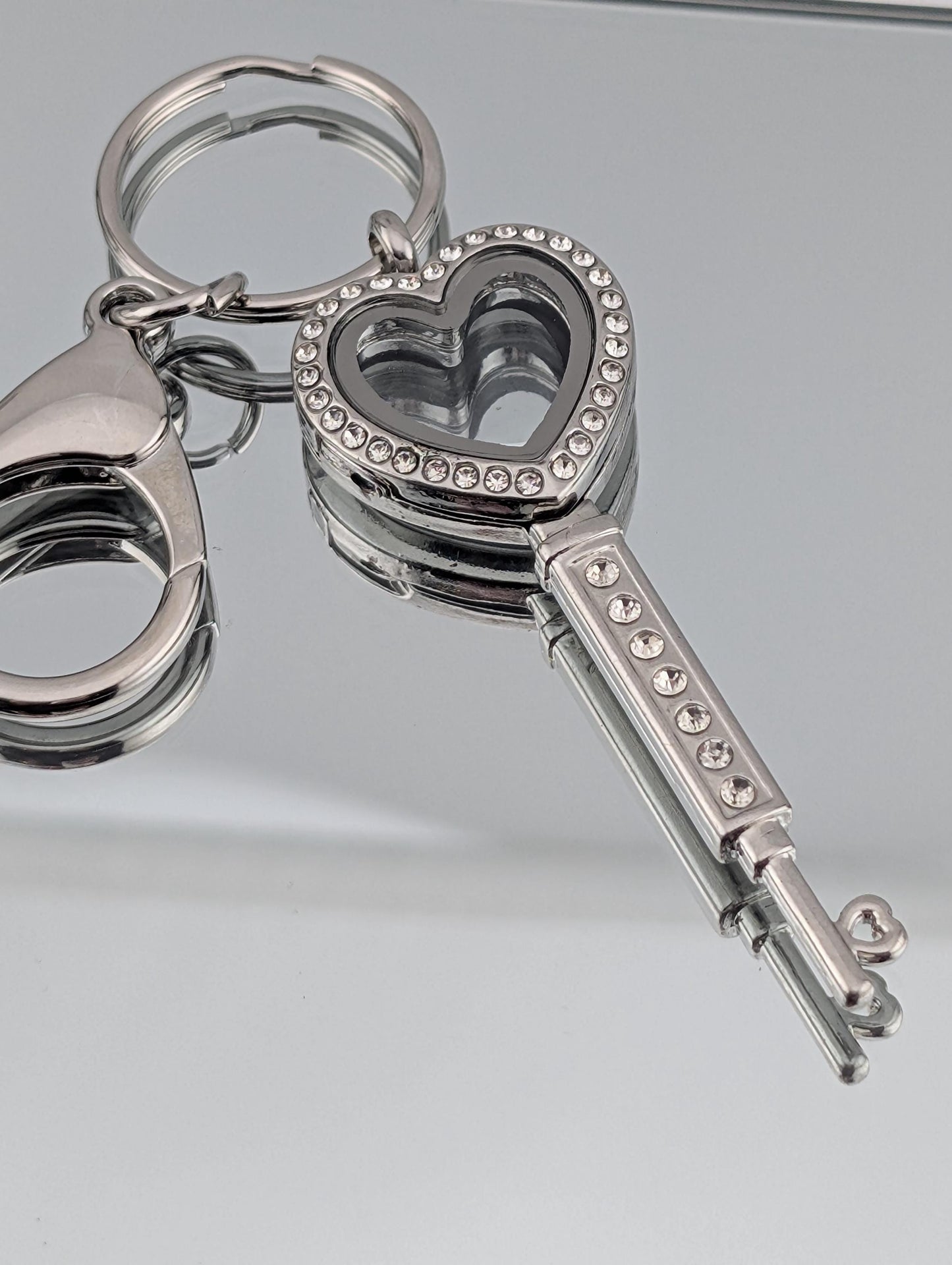A silver keychain with a heart-shaped compartment and sparkling rhinestones.