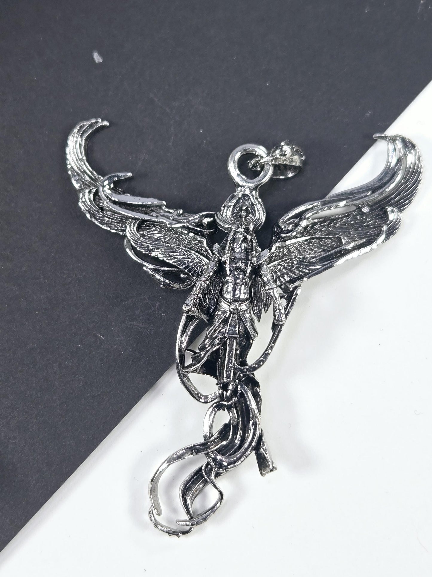 A silver-colored metal pendant in the shape of a bird, with intricate details and a decorative design.