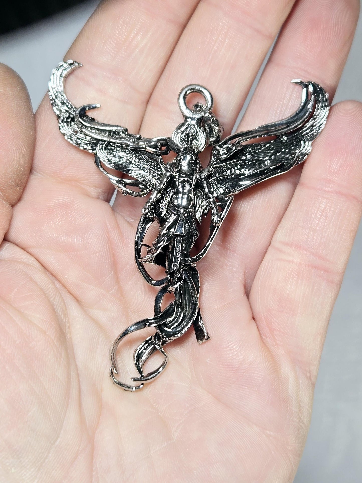 A close-up image of a person's hand holding a silver, intricately designed pendant or charm in the shape of a dragon or mythical creature.