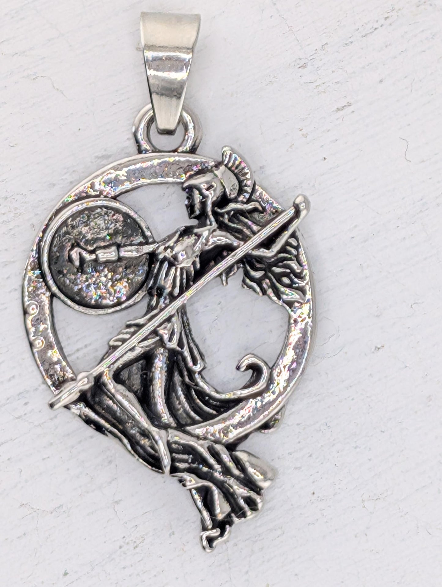 A silver-colored pendant featuring an intricate design of a woman holding a shield and a sword.
