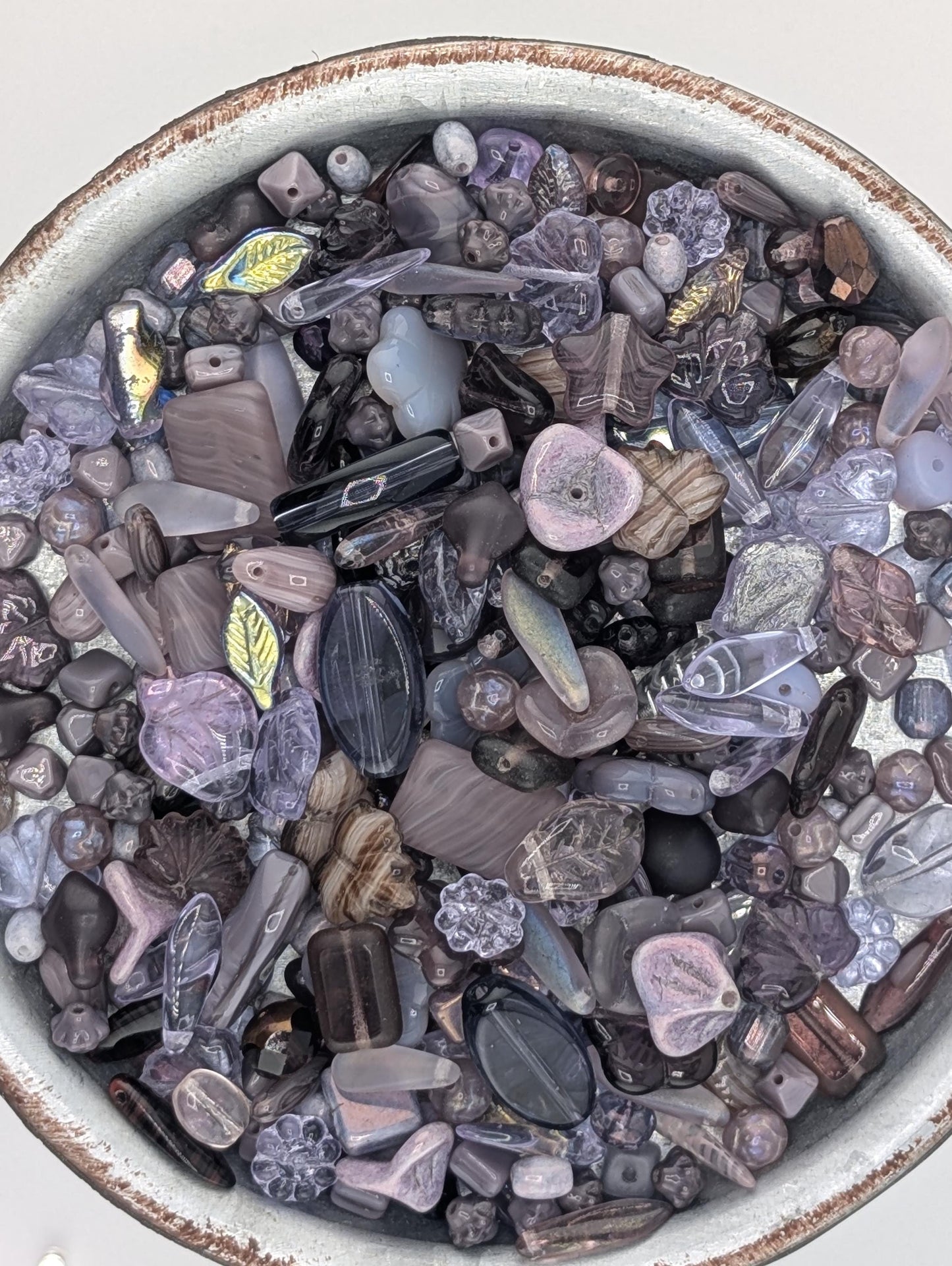 a bowl filled with various colored glass beads, including shades of purple, blue, and gray.