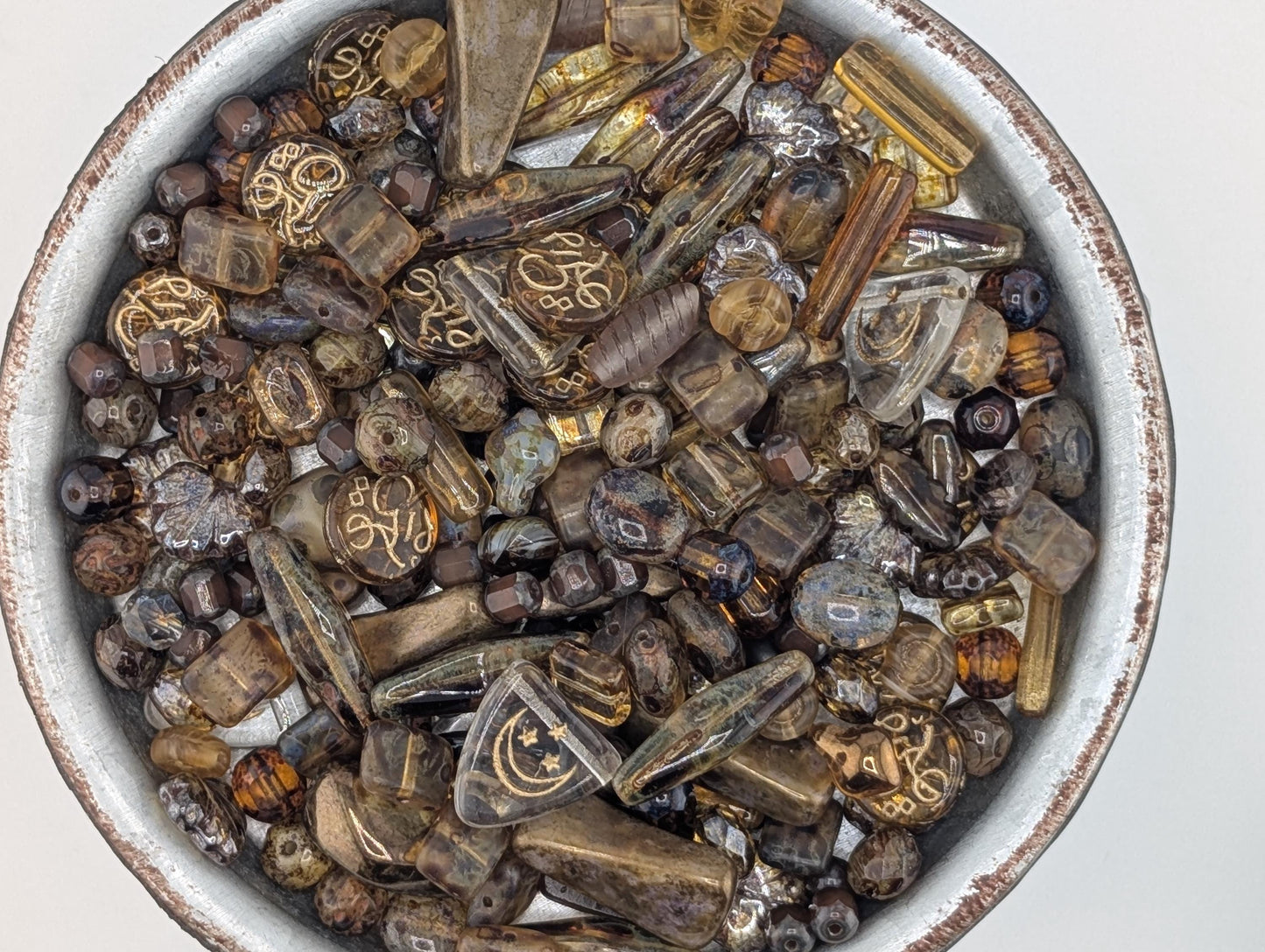 A bowl filled with various colored glass beads, including clear, brown, and multicolored pieces.