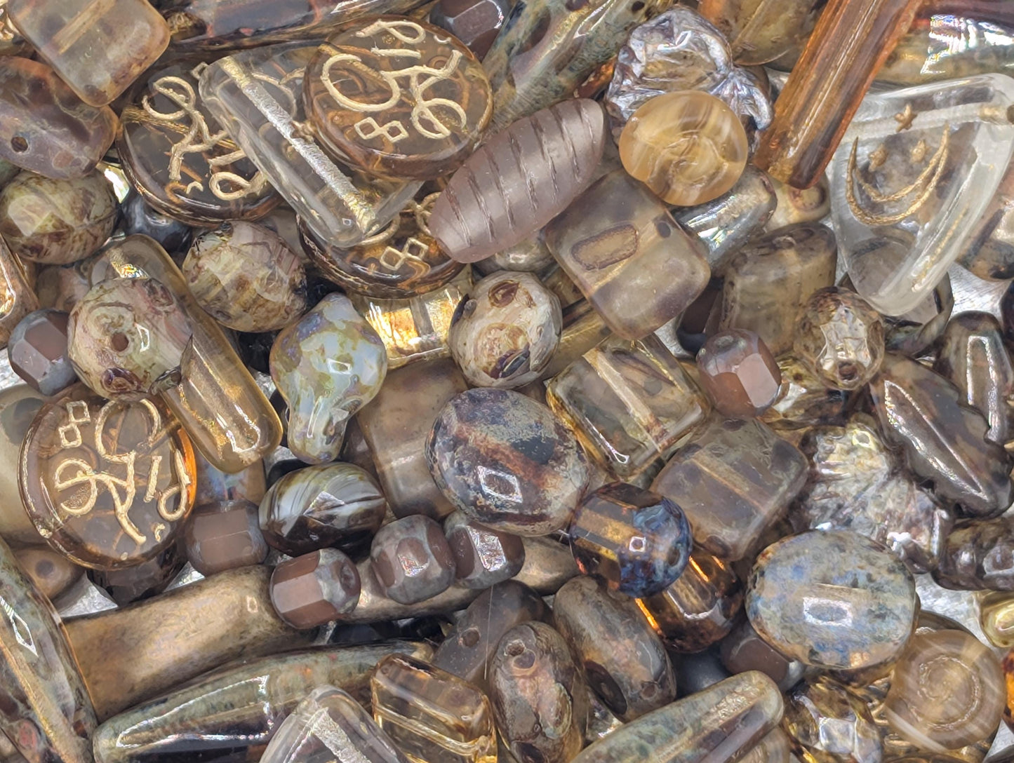 The image is a close-up of various glass beads and objects, including glass beads, glass rods, and glass pieces, all with a brownish-brown color.