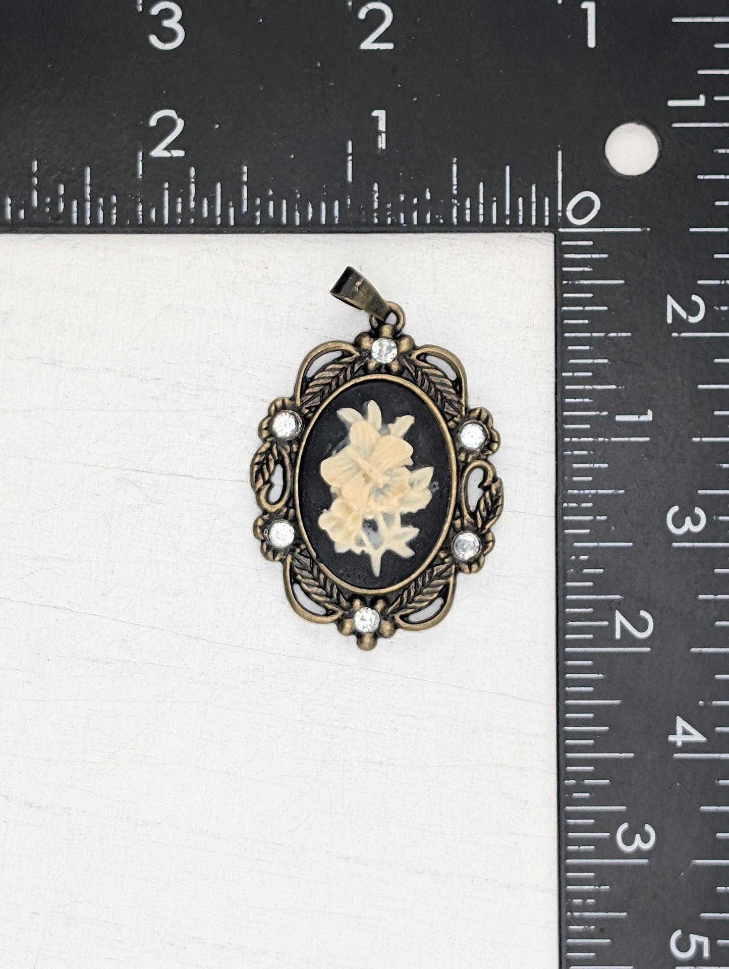 A pendant with a floral design and a small flower inside, placed next to a ruler for size comparison.