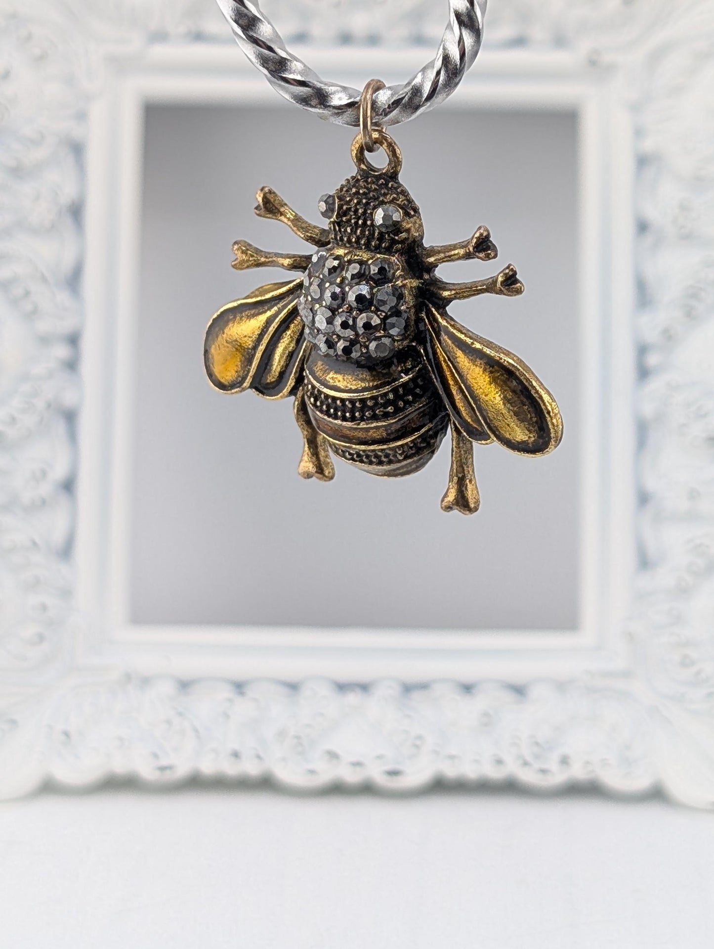 A decorative pendant in the shape of a bee, with intricate details and sparkling gemstones, is hanging from a chain.