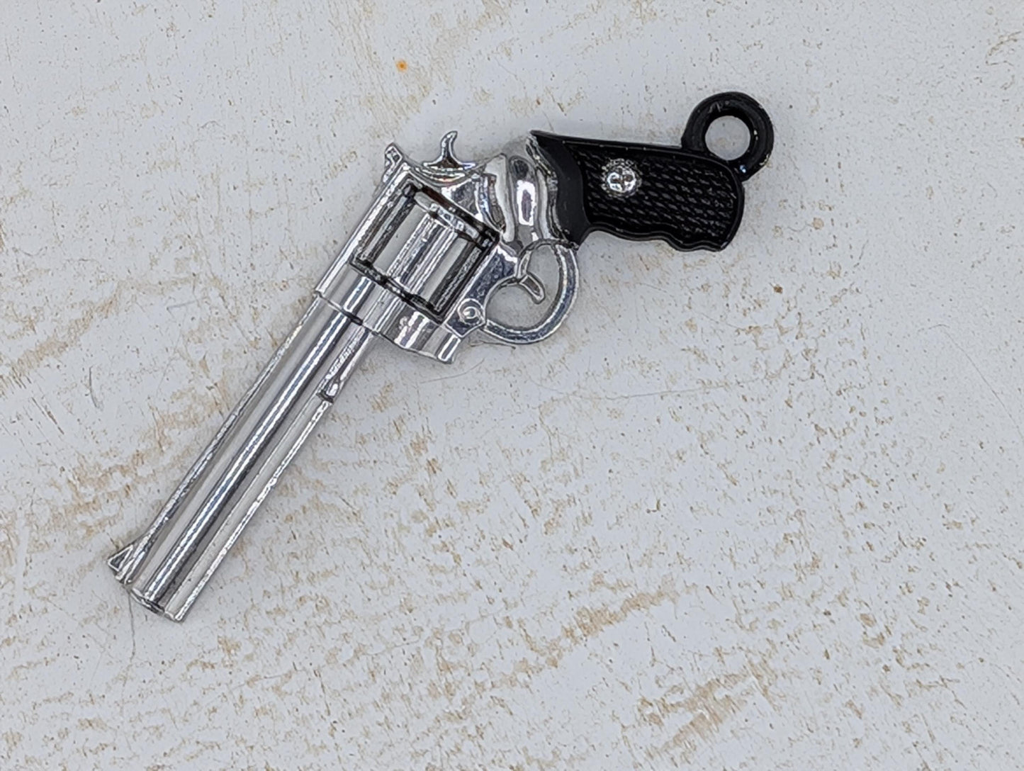 A silver toy gun with a black grip is lying on a white surface.