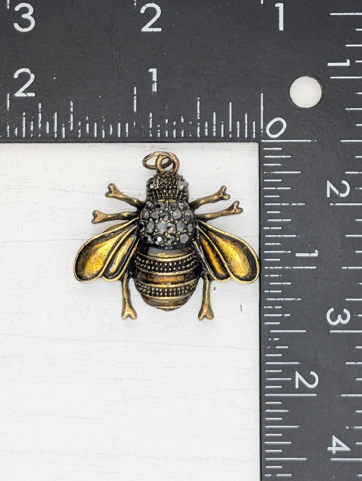 A close-up image of a decorative metal bee pendant with a diamond-encrusted design.