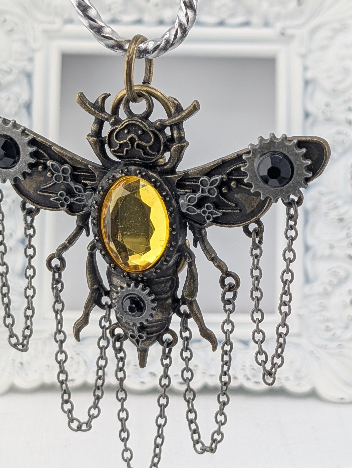 A decorative pendant in the shape of a bee, with a yellow gemstone in the center and intricate metalwork detailing.