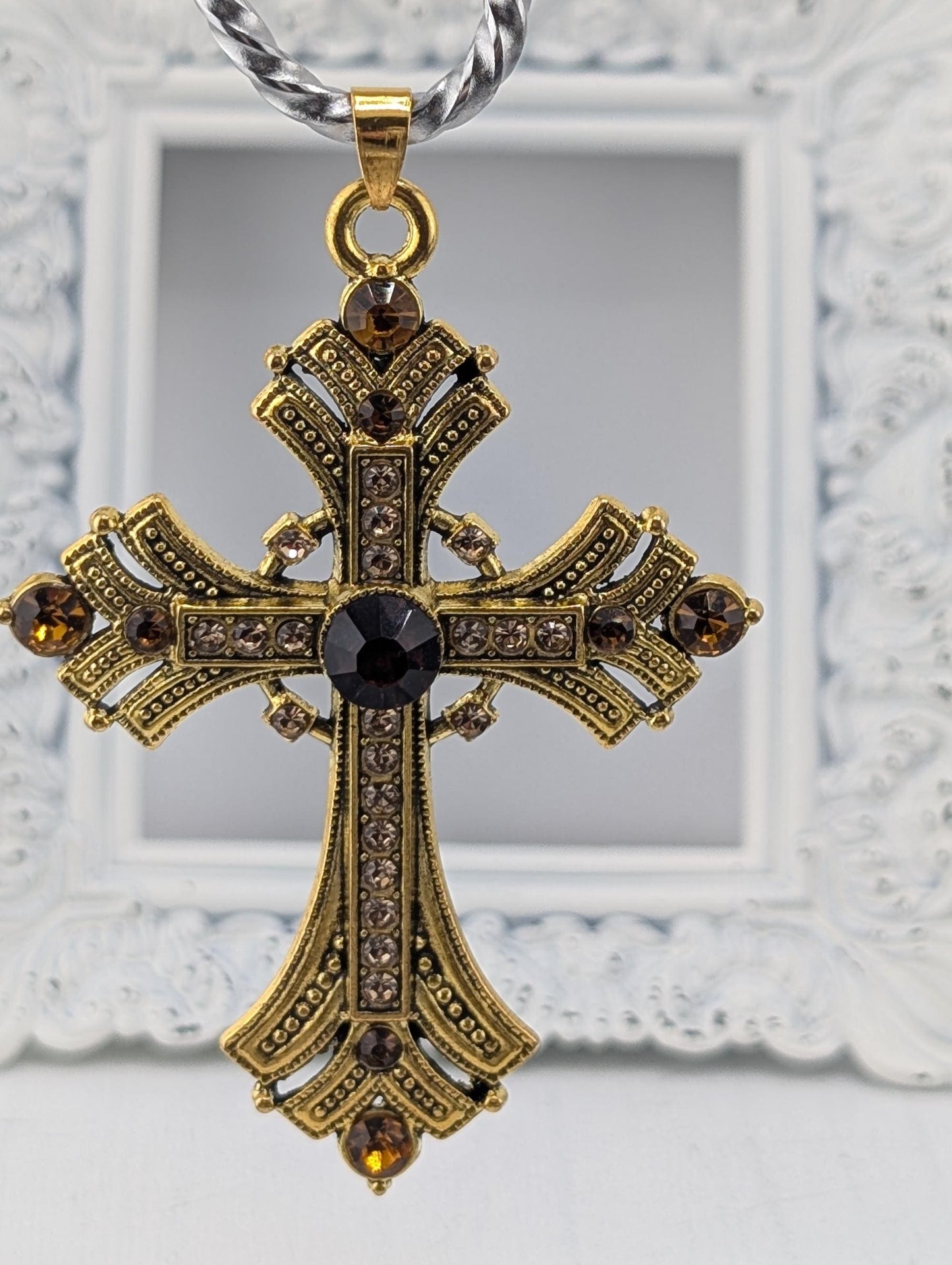 A decorative gold cross pendant with a dark stone at the center, hanging from a silver chain.