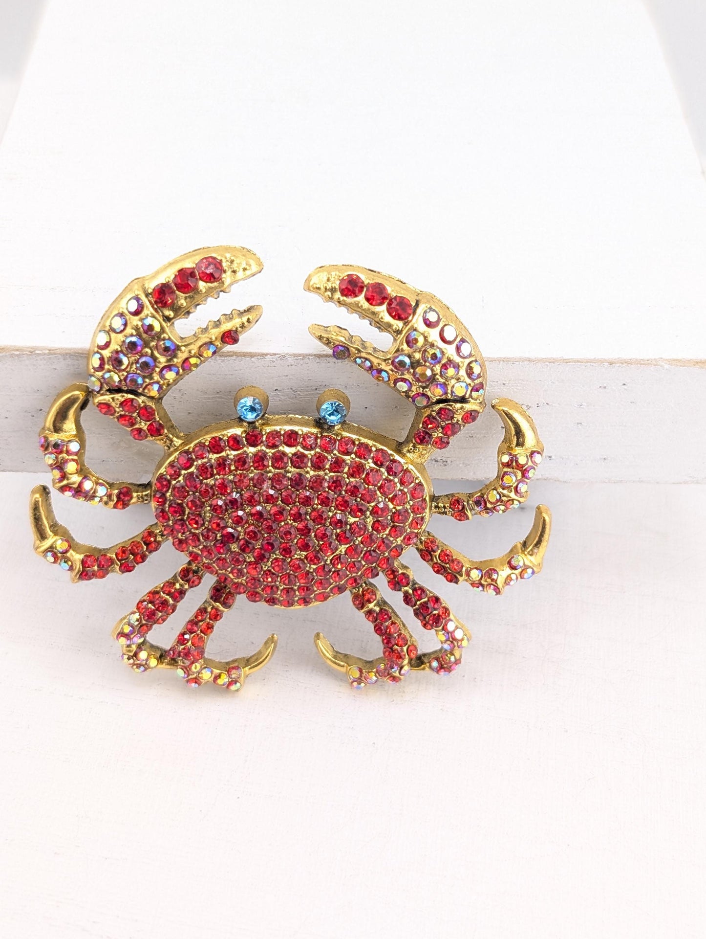 A decorative crab brooch with a red and gold color scheme, adorned with numerous sparkling gemstones.