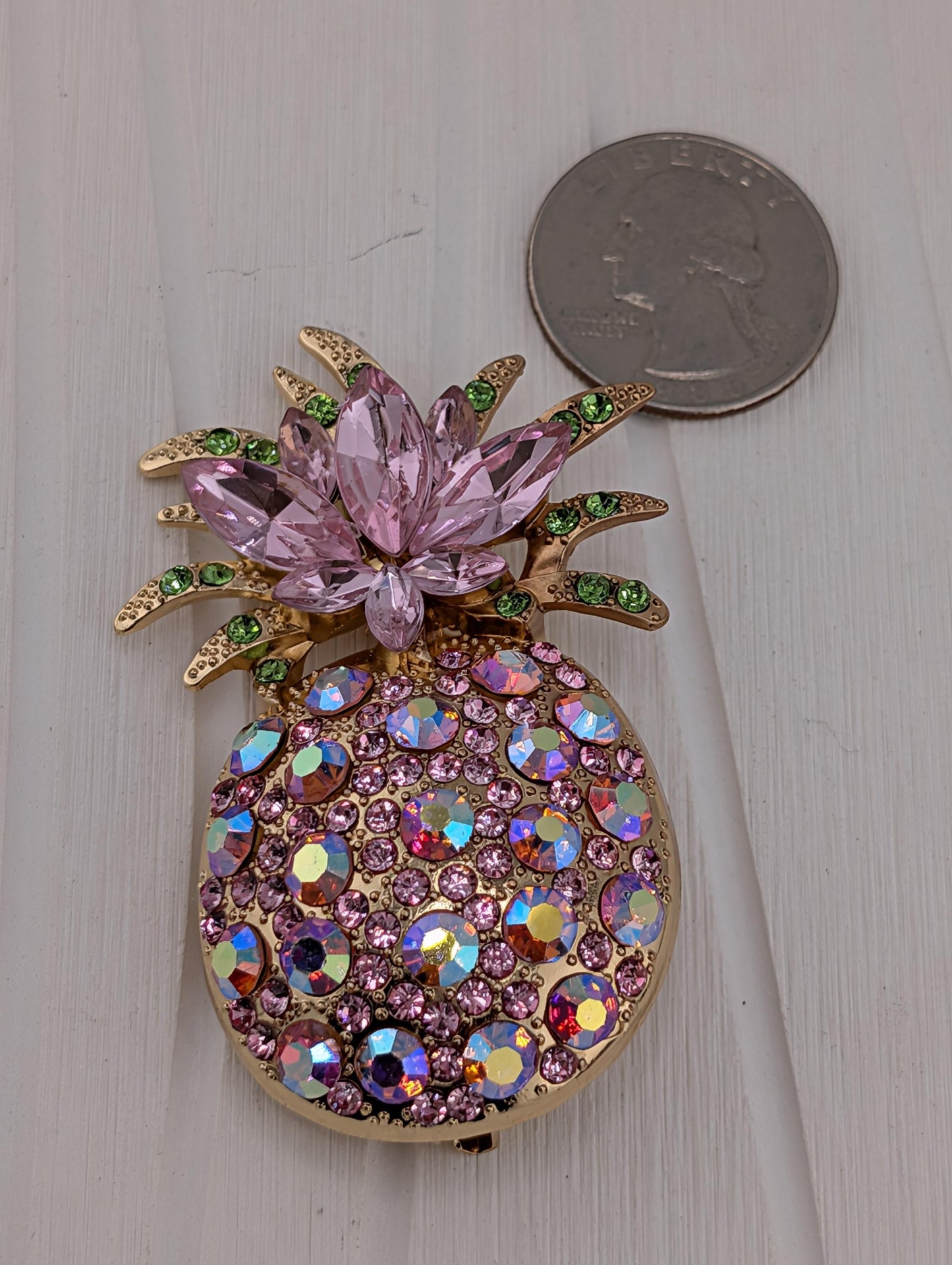 A decorative pineapple-shaped brooch adorned with numerous sparkling purple and green gemstones.
