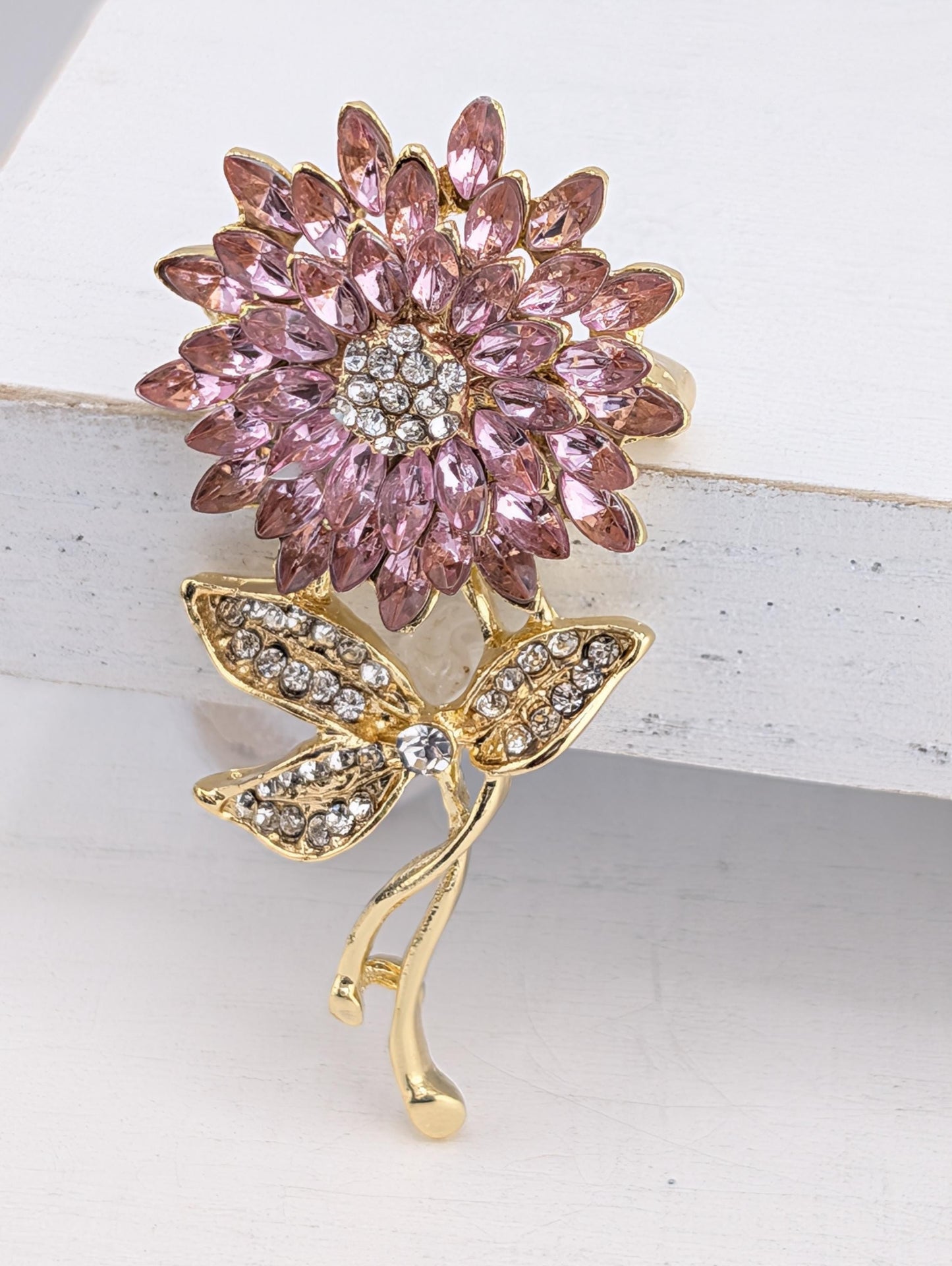 A decorative brooch with a pink flower design and sparkling gemstones.
