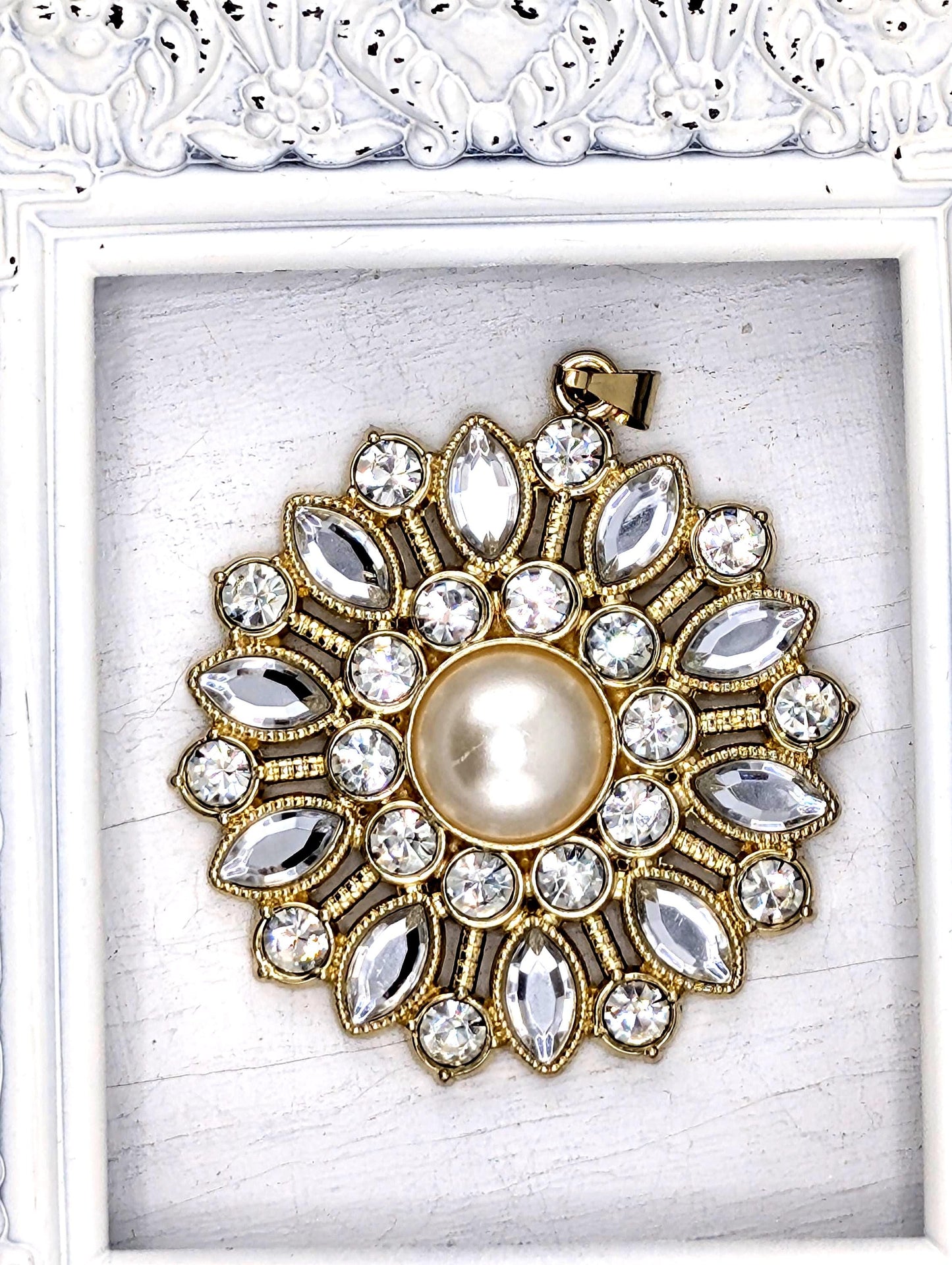 A decorative pendant with a large pearl at its center, surrounded by numerous sparkling gemstones in a gold and white design.