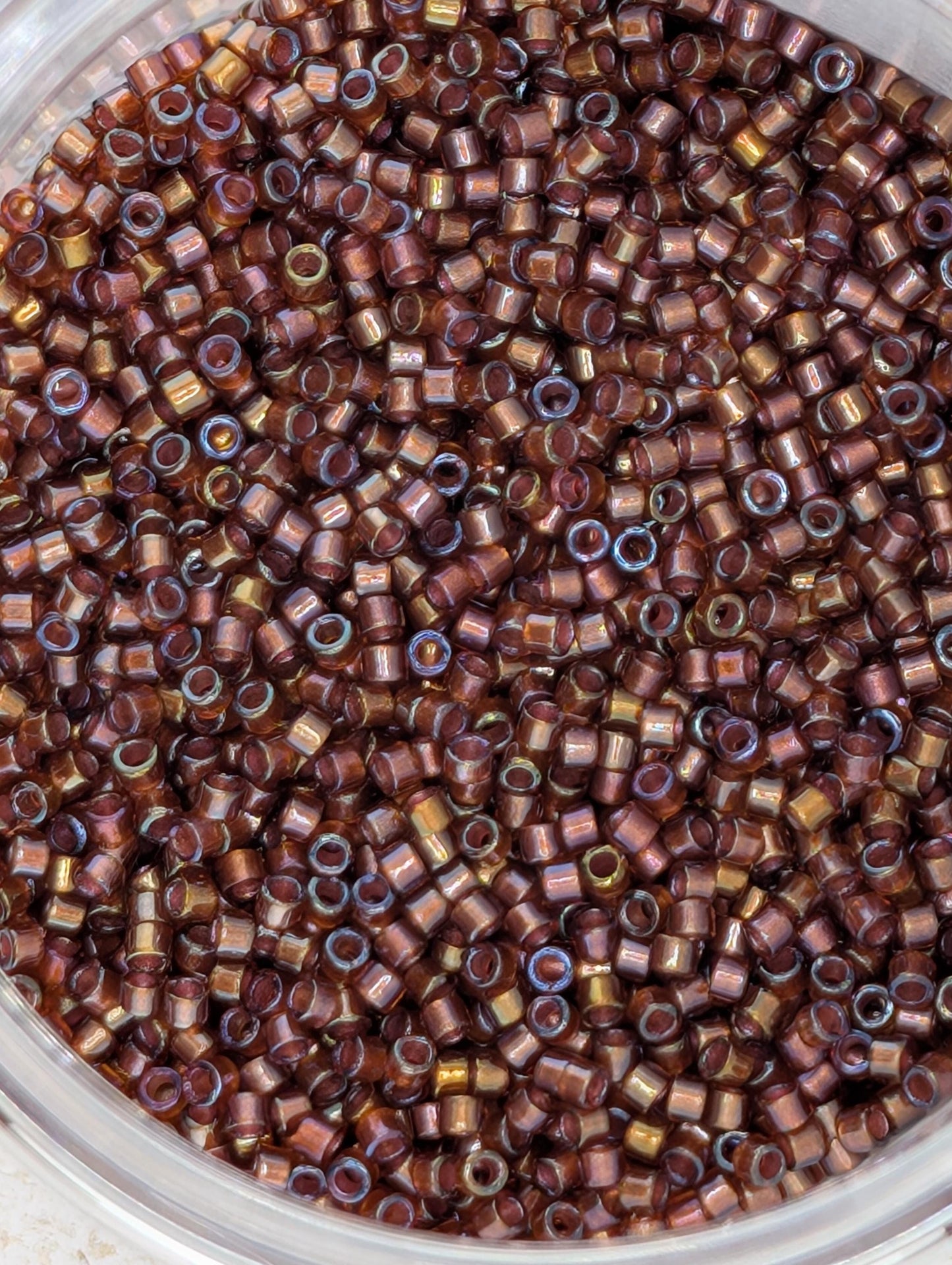 A close-up image of a container filled with numerous small, round beads in various shades of brown and gold.