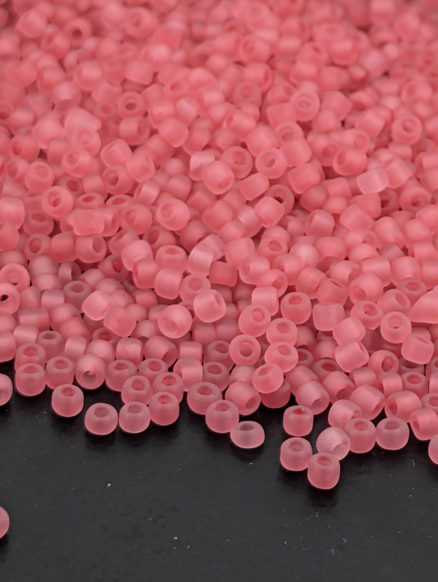 a close-up view of numerous small, clear beads in a soft pink color, scattered across a dark surface.
