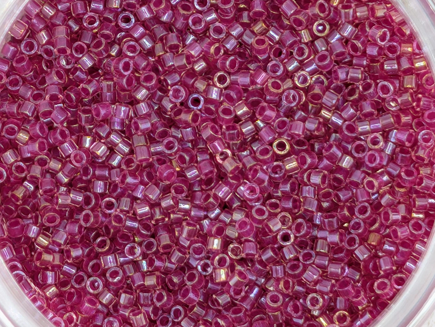 A close-up image of a container filled with numerous small, round beads in a vibrant shade of pink.