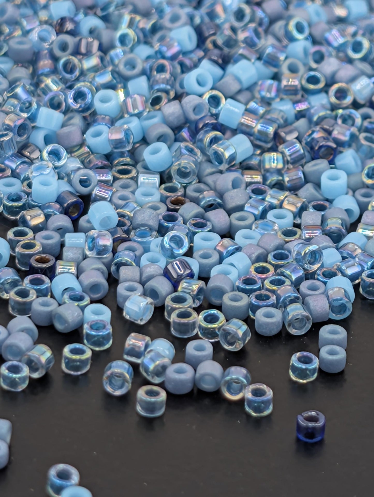 a large pile of small, clear beads in various shades of blue and gray, scattered on a dark surface.