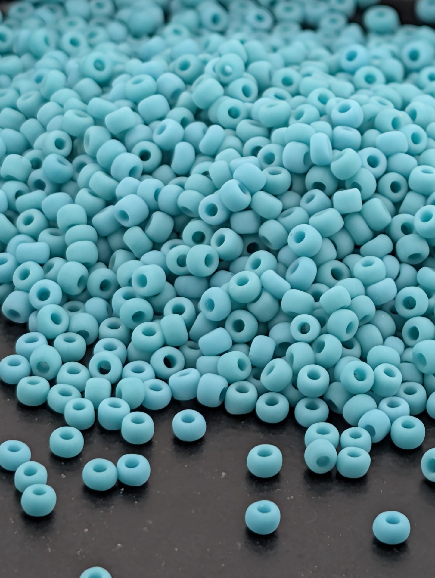 A pile of small, light blue beads scattered on a dark surface.
