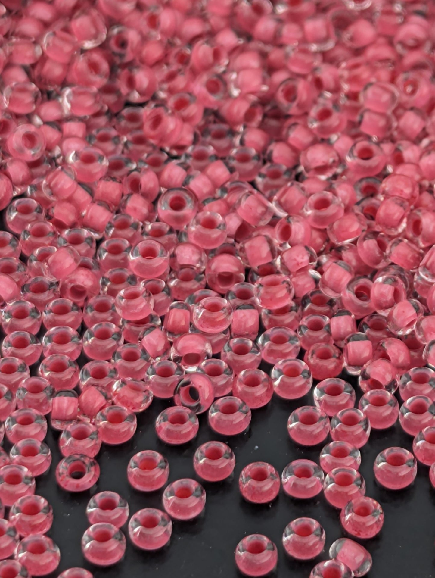 The image is a close-up of numerous clear glass beads in a pink color, scattered across a dark background.